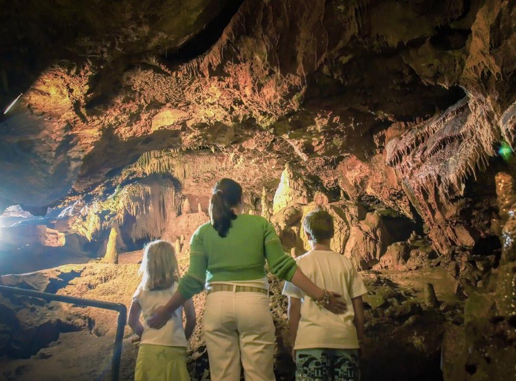 A woman and two children exploring the inside of Kents Cavern, surrounded by rocky cave walls and formations.