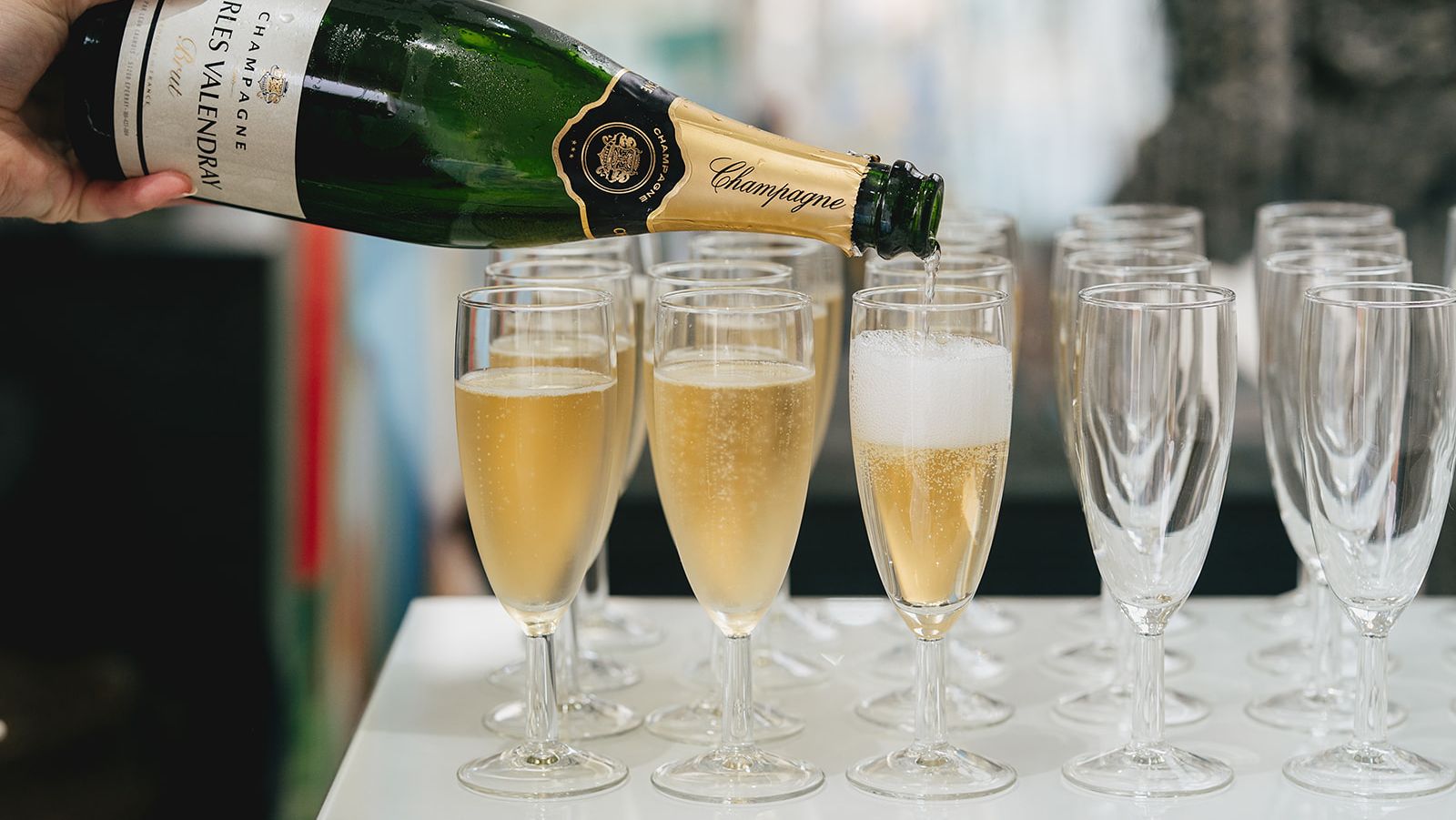 Champagne being poured from a bottle into a row of champagne flutes.