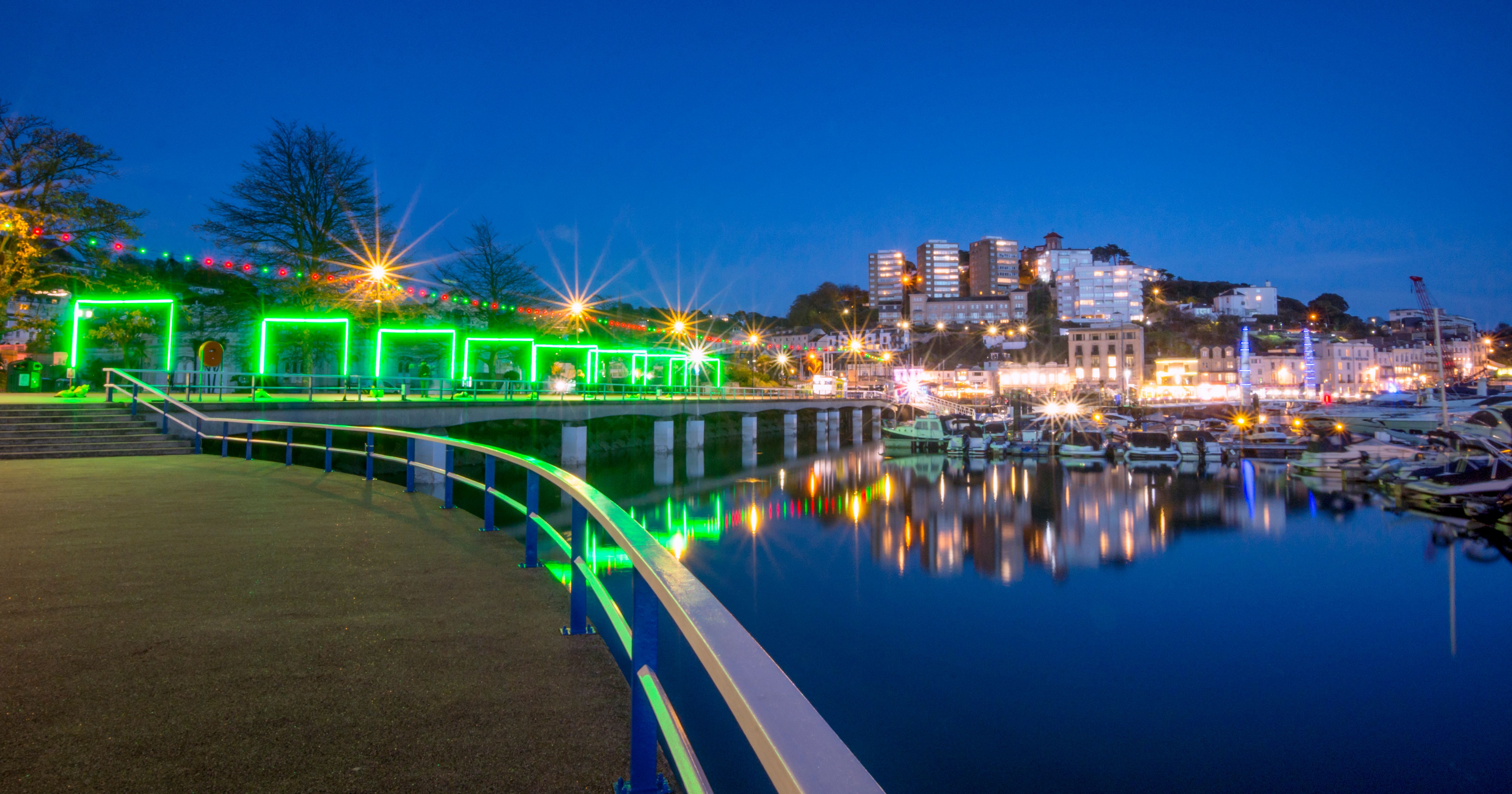 Torquay Marina illuminated with green lights and colorful reflections at night during the Bay of Lights event.