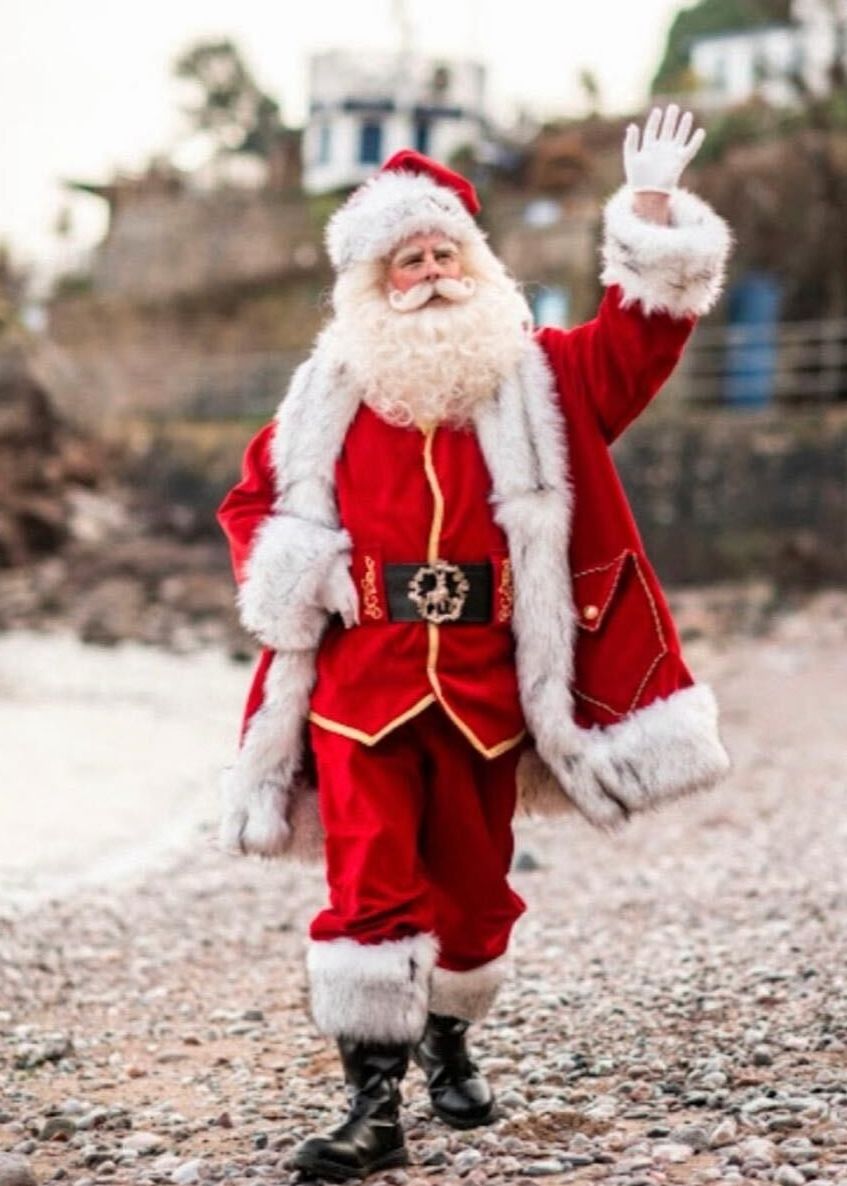 Santa Claus waving while walking on a rocky beach