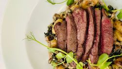 Sliced steak served on creamy gnocchi with fresh greens, presented on a white plate.