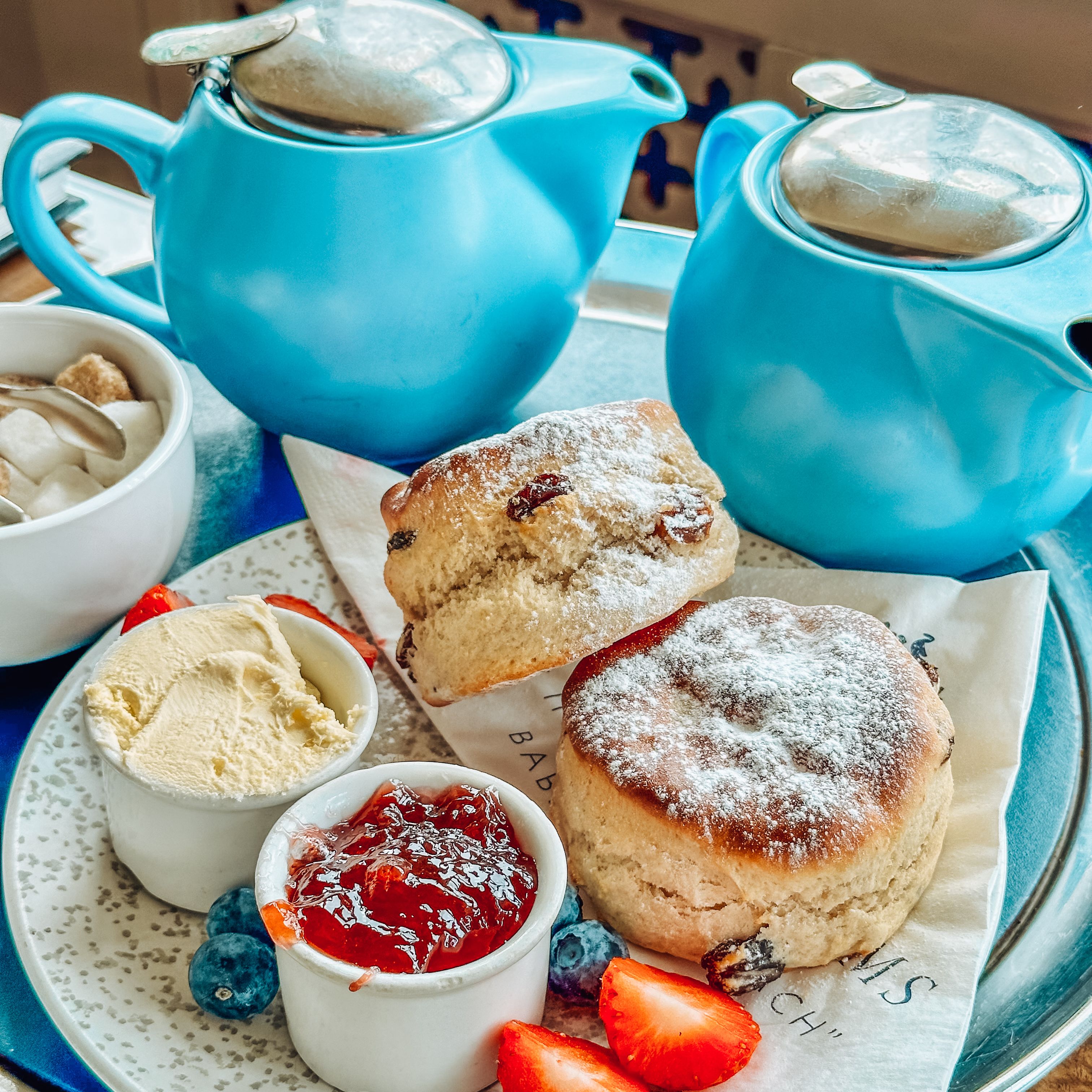 Afternoon tea with scones, clotted cream, jam, strawberries, blueberries, and blue teapots