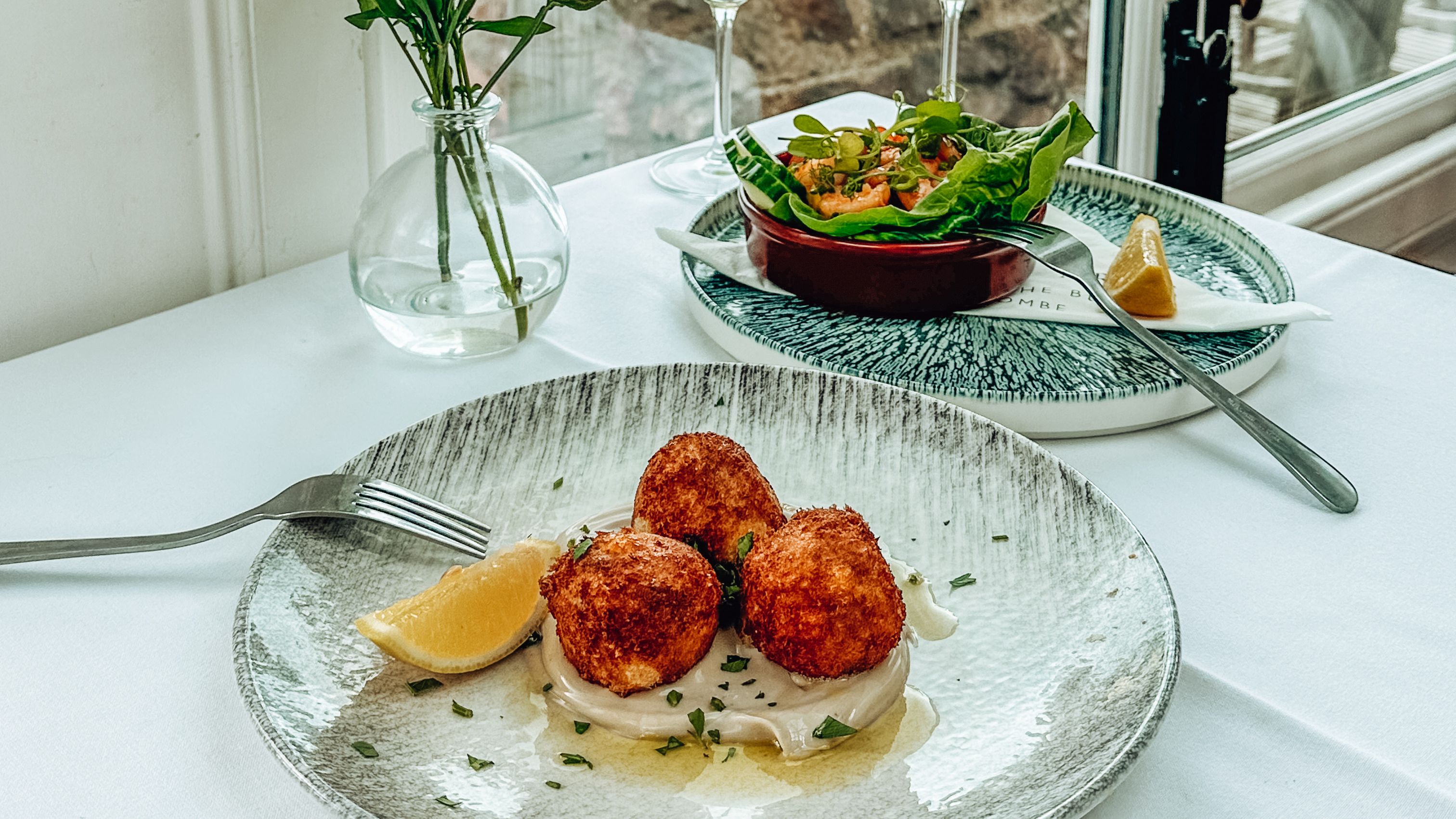 Table set with gourmet seafood appetizers, white wine glasses, and a seaside view.