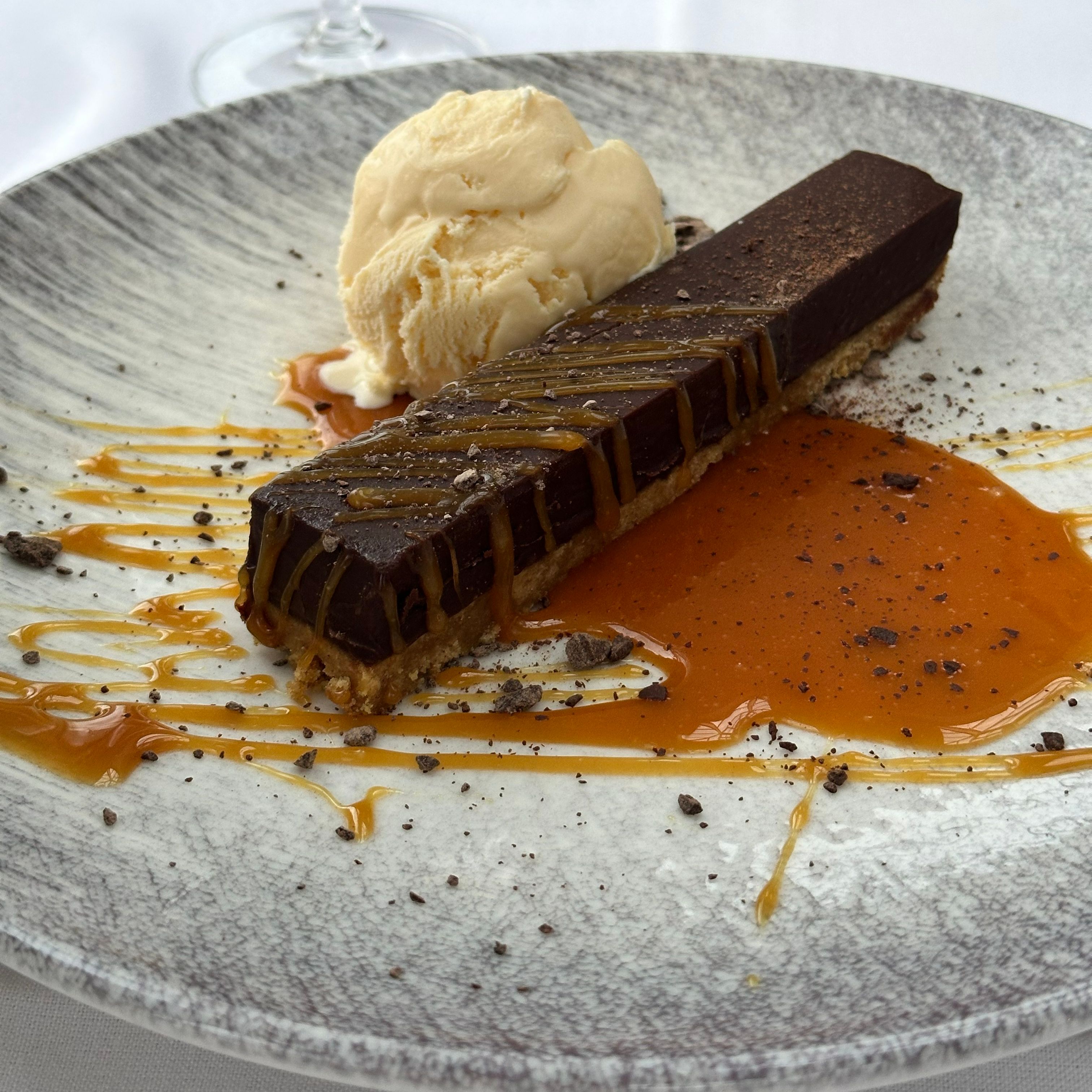 Chocolate tart with caramel drizzle and a scoop of vanilla ice cream on a decorative plate.