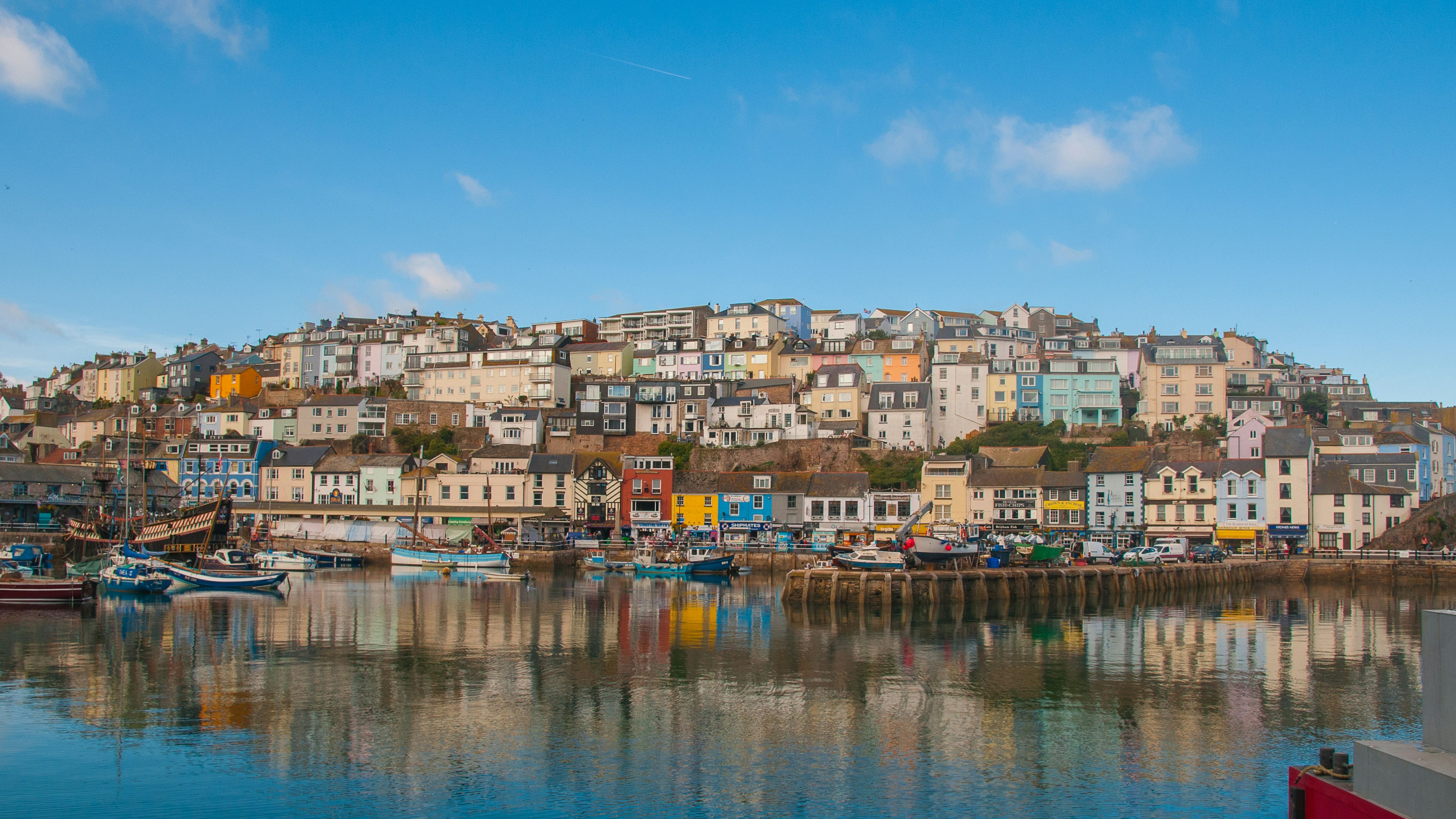 Colorful houses on a hillside overlooking a harbor with boats, reflected in the water under a blue sky.