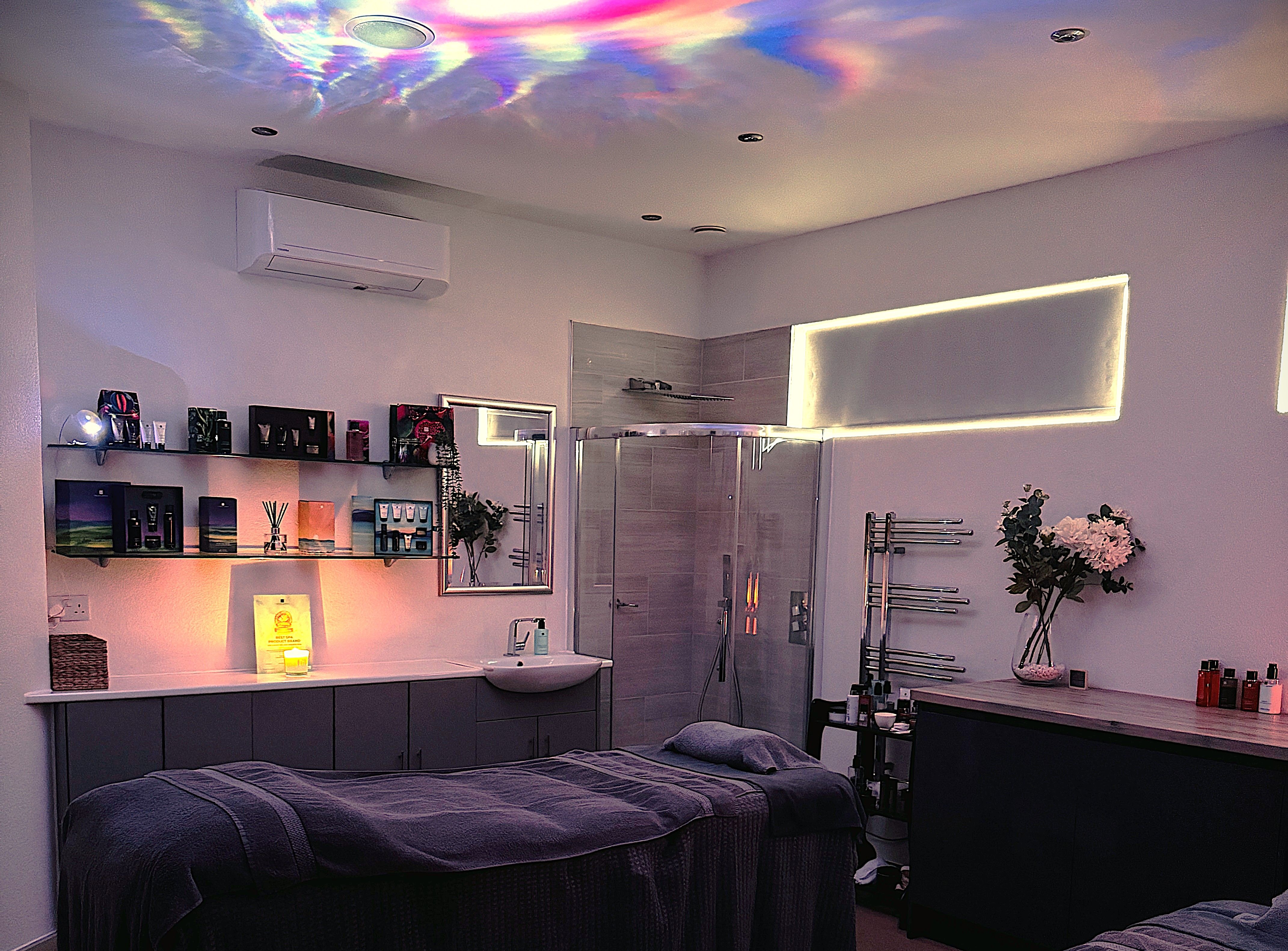 A tranquil spa room with two massage tables, dim lighting, and colorful lights reflected on the ceiling.