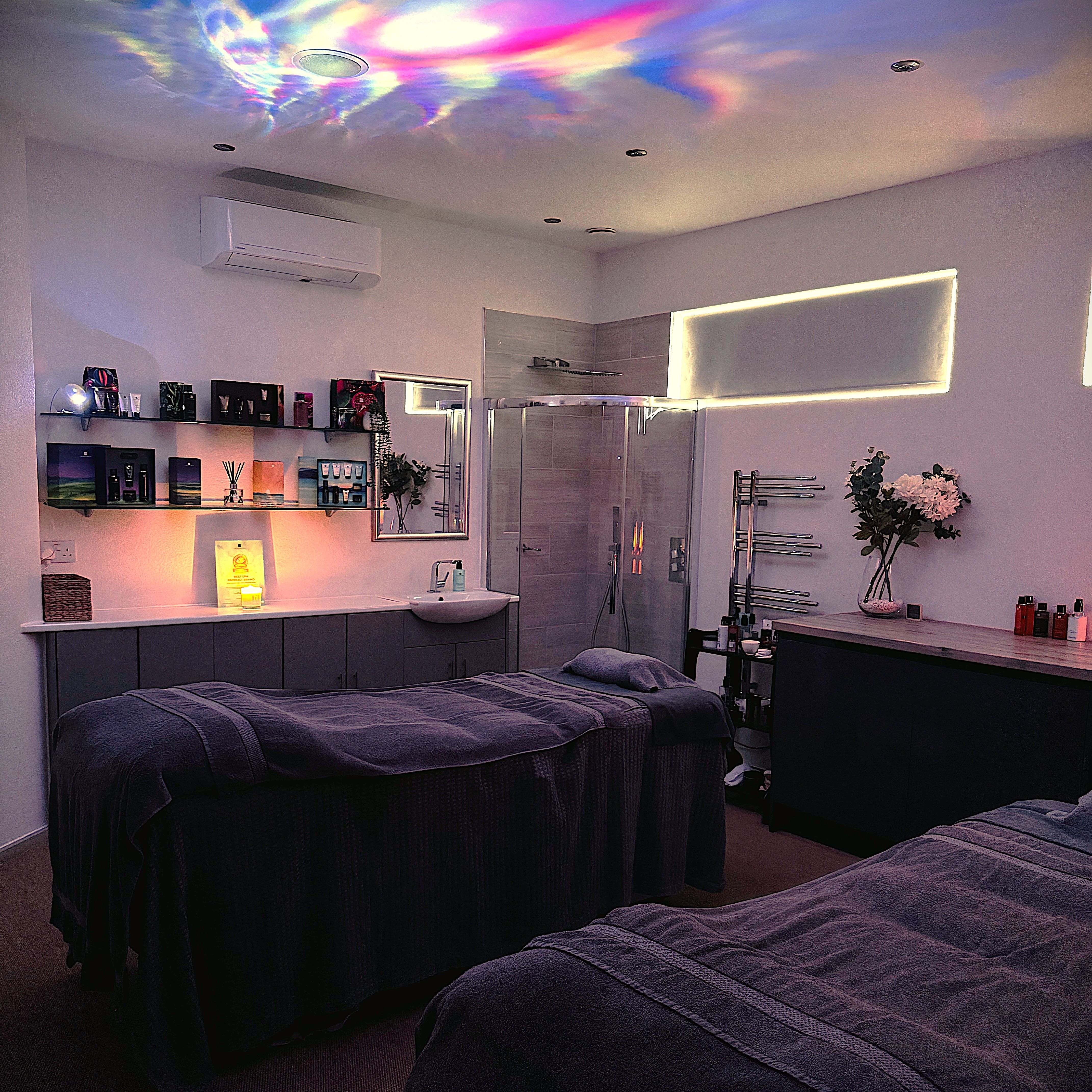 A tranquil spa room with two massage tables, dim lighting, and colorful lights reflected on the ceiling.