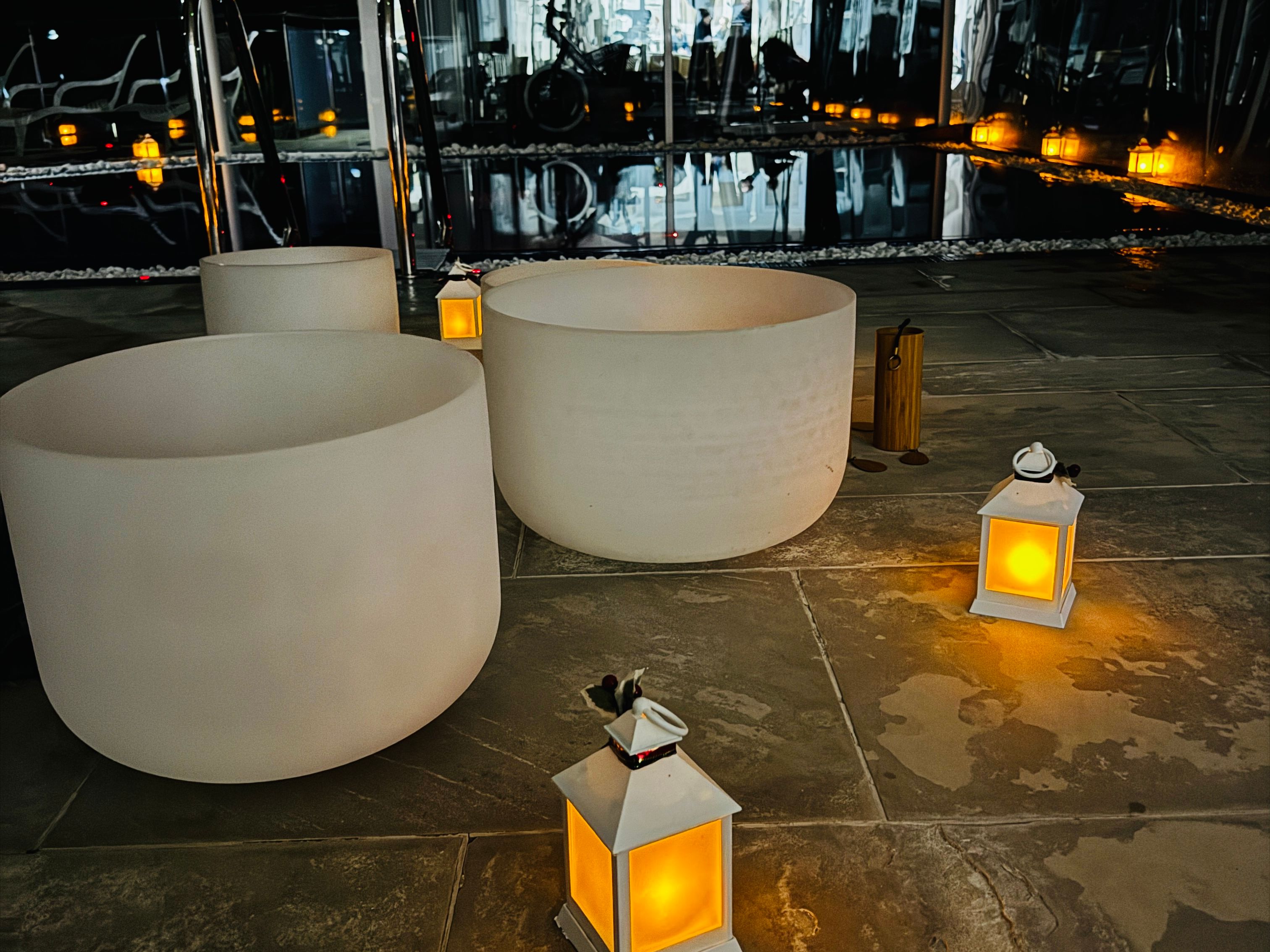 Indoor spa area with glowing lanterns and white singing bowls near a reflective swimming pool at night.