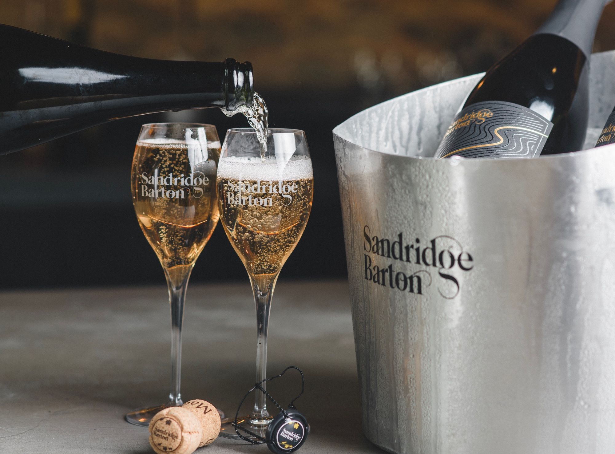 Sandridge Barton sparkling wine being poured into two glasses beside a chilled wine bucket and cork.