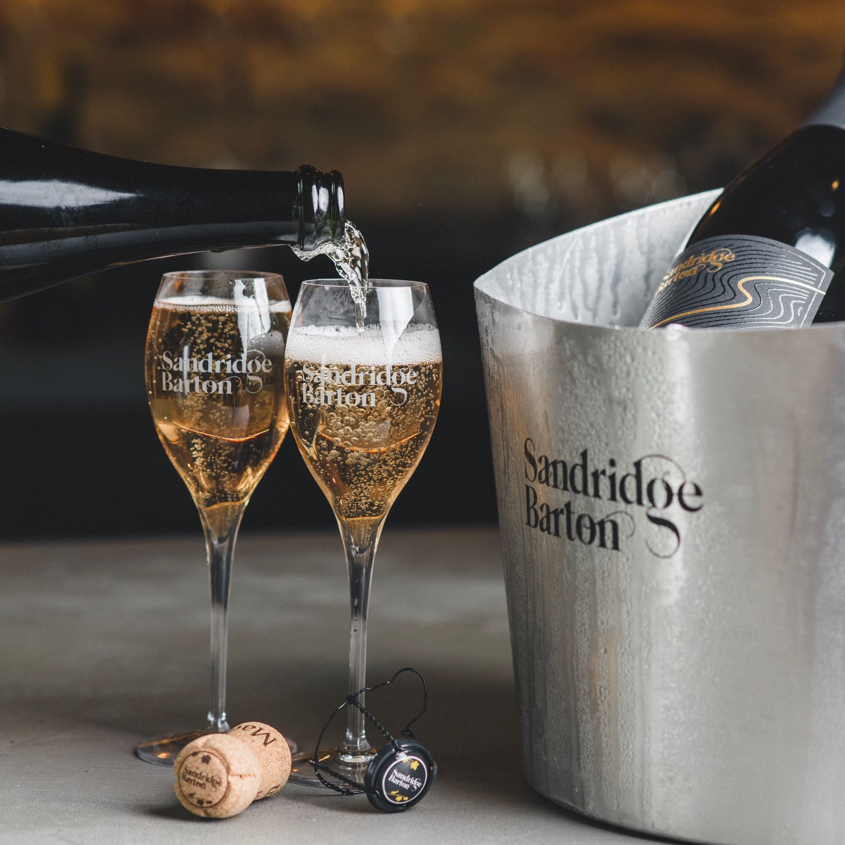 Sandridge Barton sparkling wine being poured into two glasses beside a chilled wine bucket and cork.