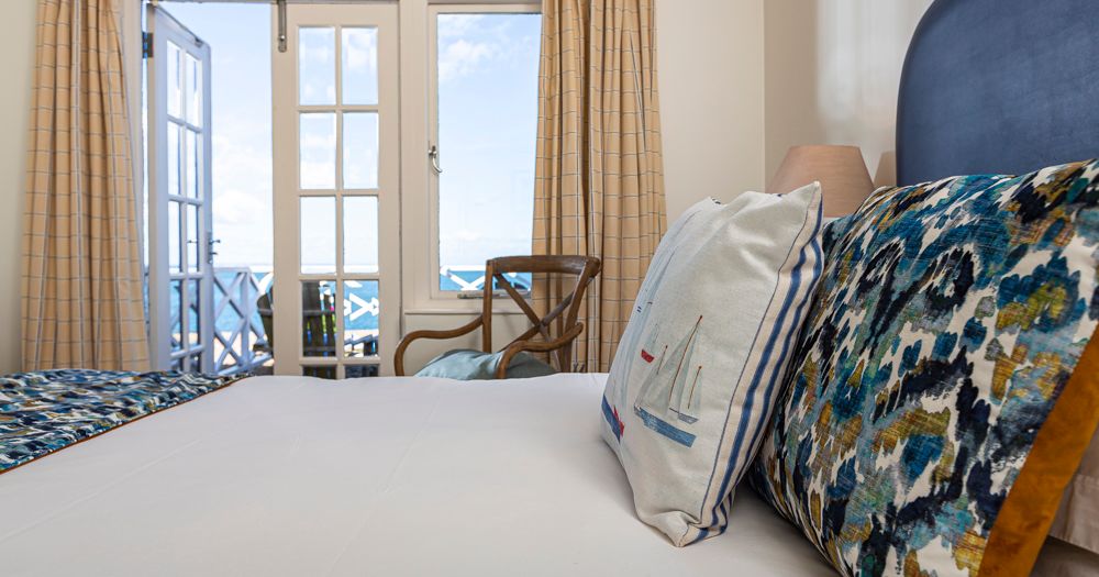 Bright bedroom with patterned cushions and open French doors leading to a balcony with sea view