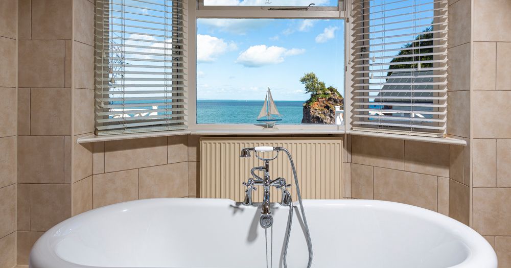 Bathtub in tiled bathroom with window view of the sea and a sailboat