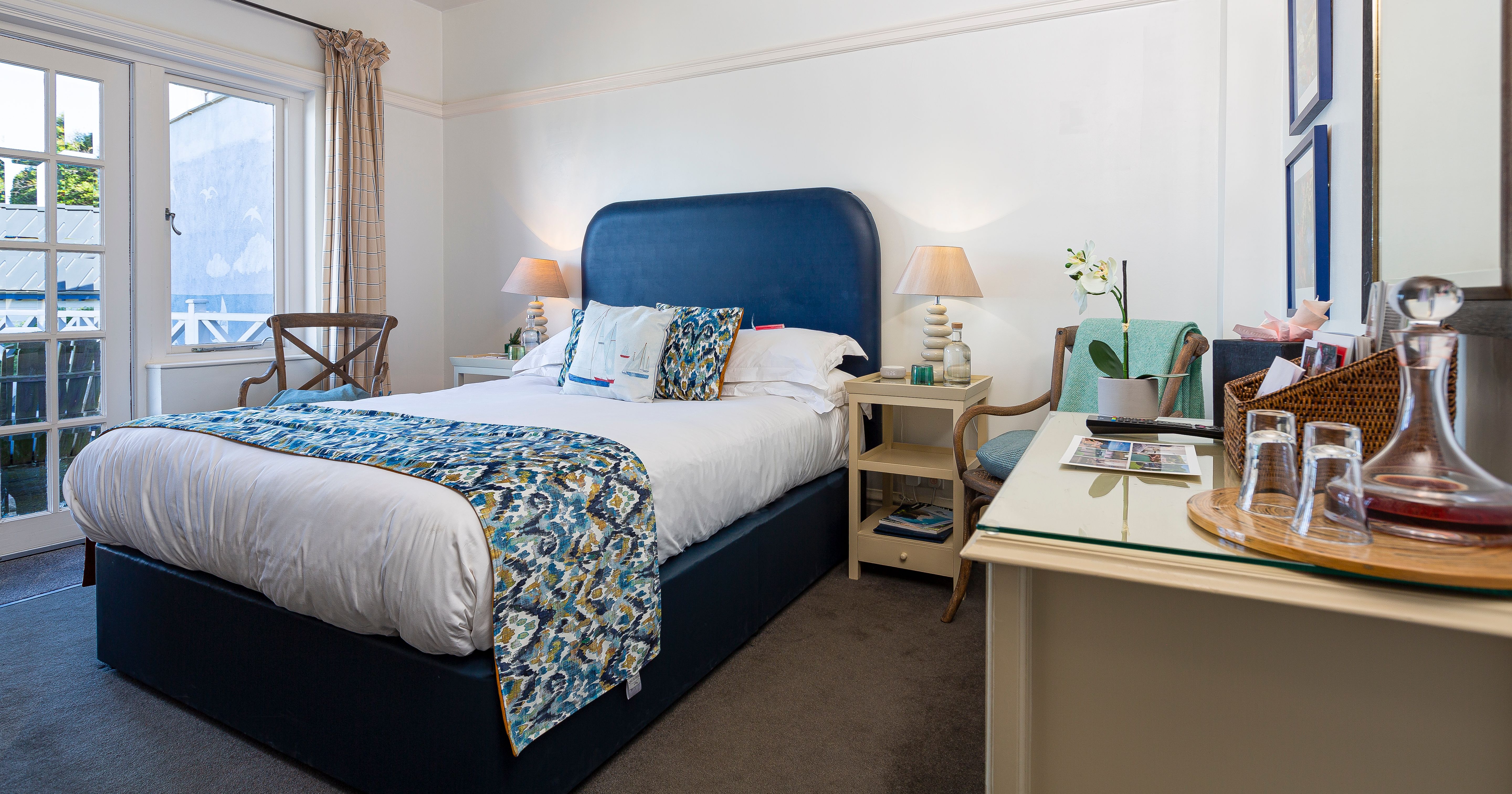 Bright bedroom with navy upholstered bed, patterned throw and bedside lamps, beside French doors