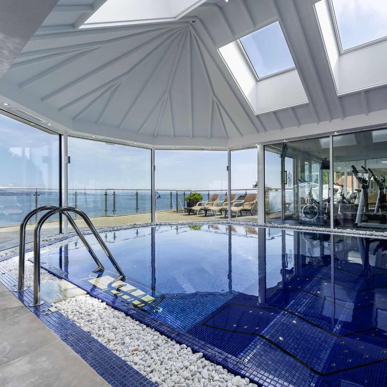 Indoor swimming pool in a glass-walled conservatory with skylights and sea view
