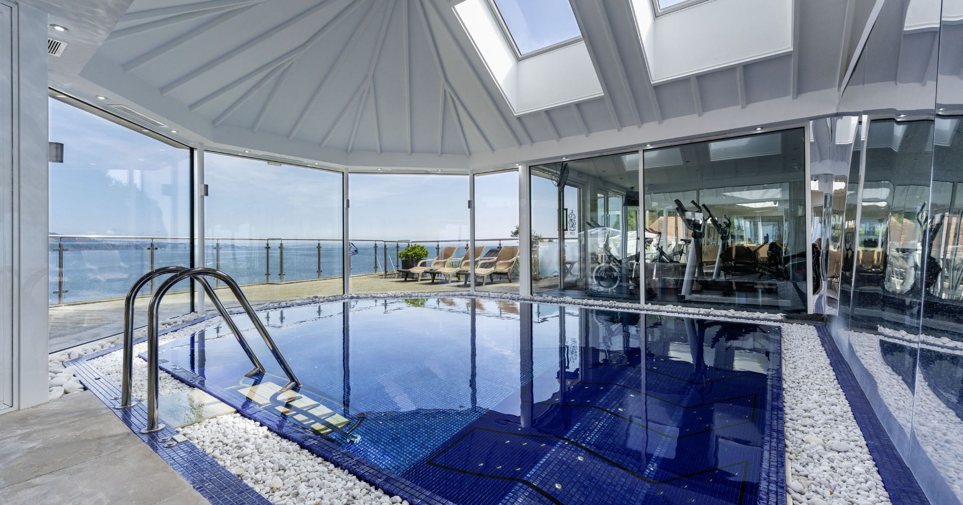 Indoor swimming pool in a glass-walled conservatory with skylights and sea view