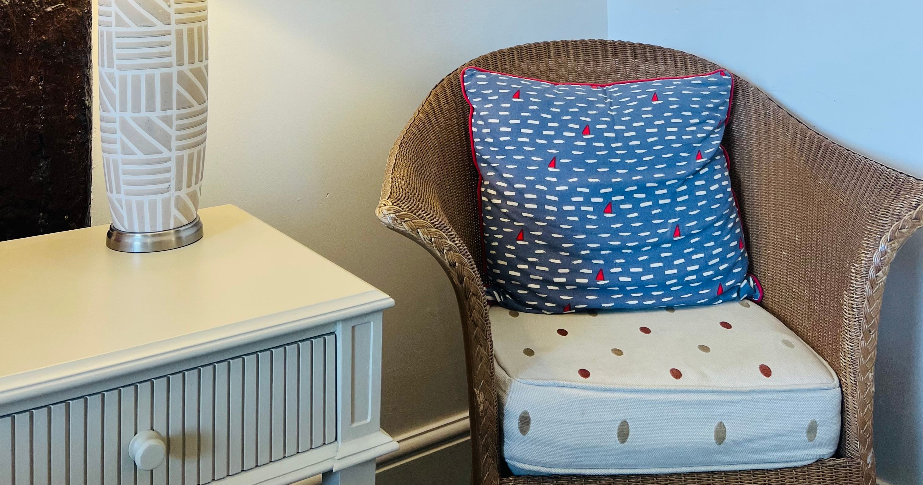 Cosy corner with a table lamp, two red-framed sea life prints, and a wicker chair with a patterned cushion