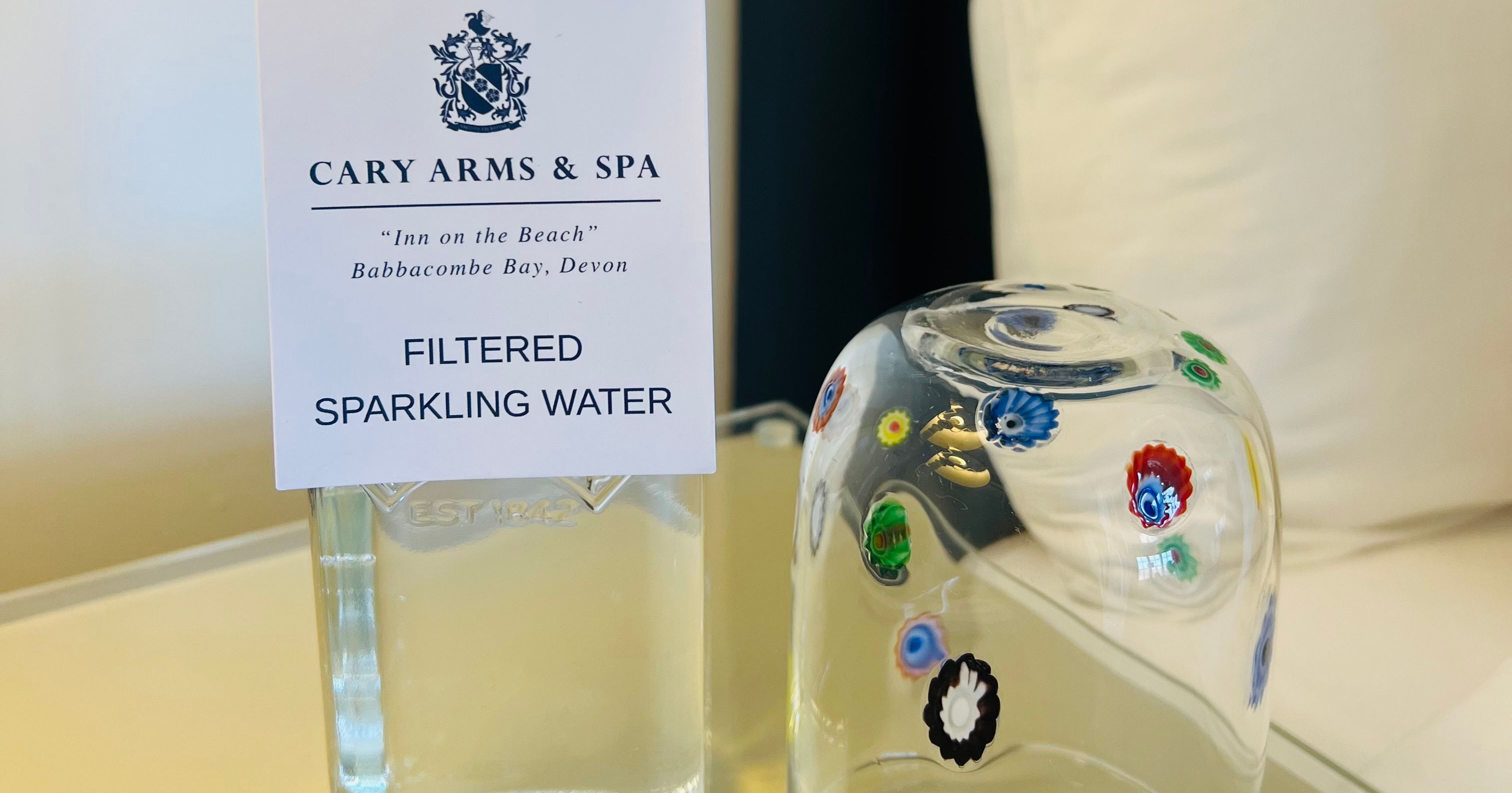 Bottle of filtered sparkling water with a swing-top cap beside an inverted decorative glass on a bedside table