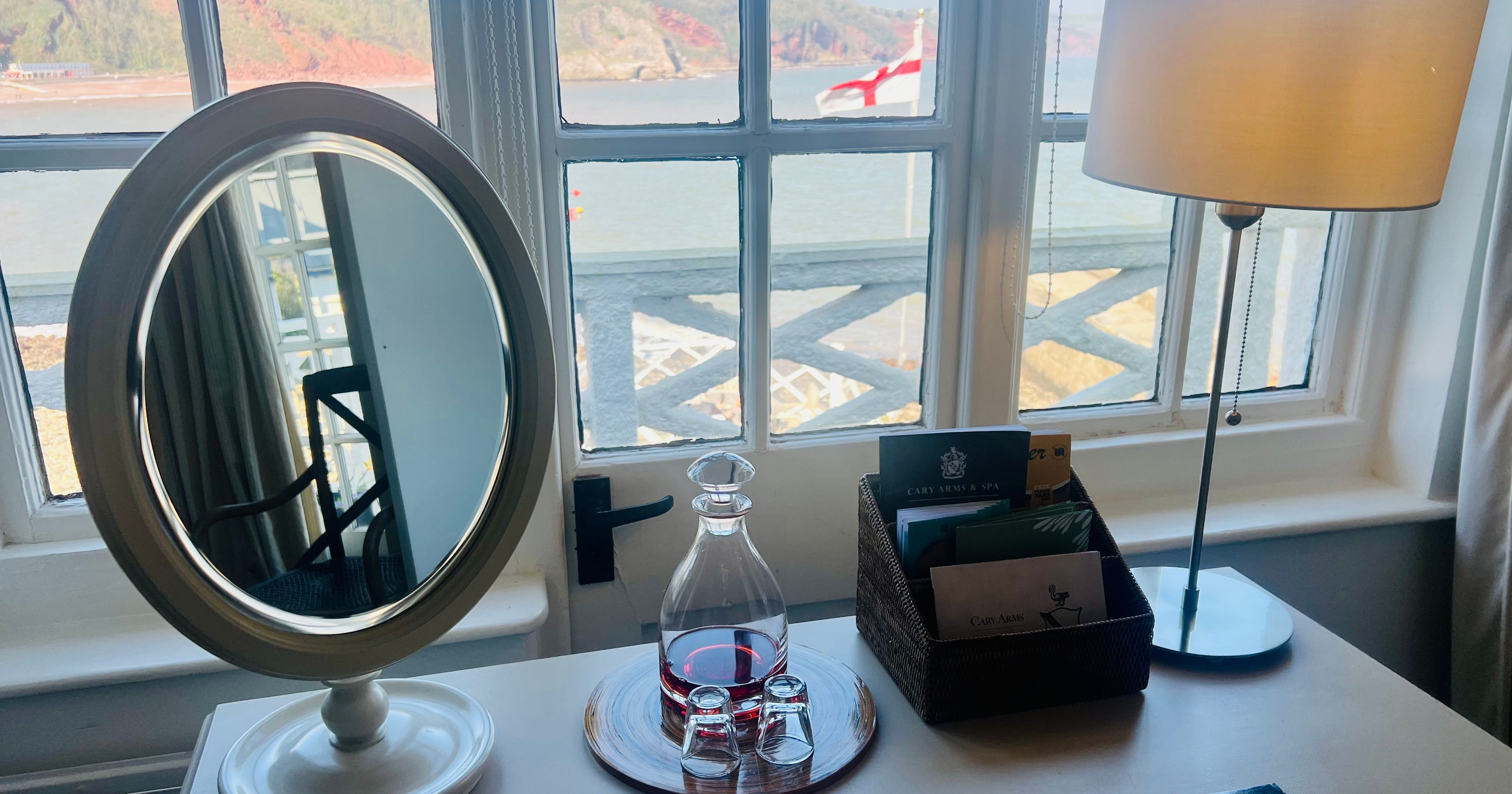 Dressing table with mirror, lamp and water carafe by a window overlooking the sea and cliffs