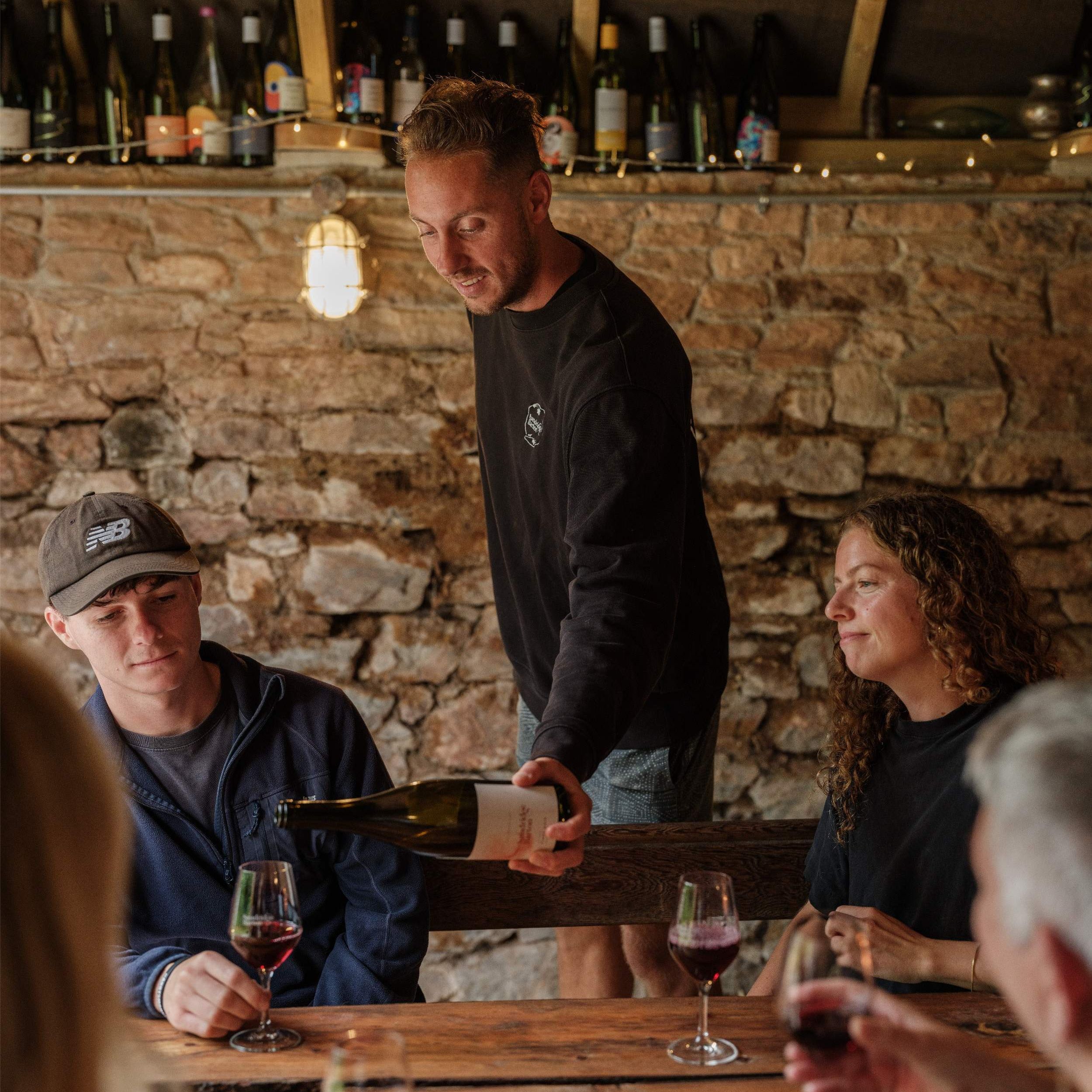 Person pouring red wine into a glass at a rustic indoor tasting table