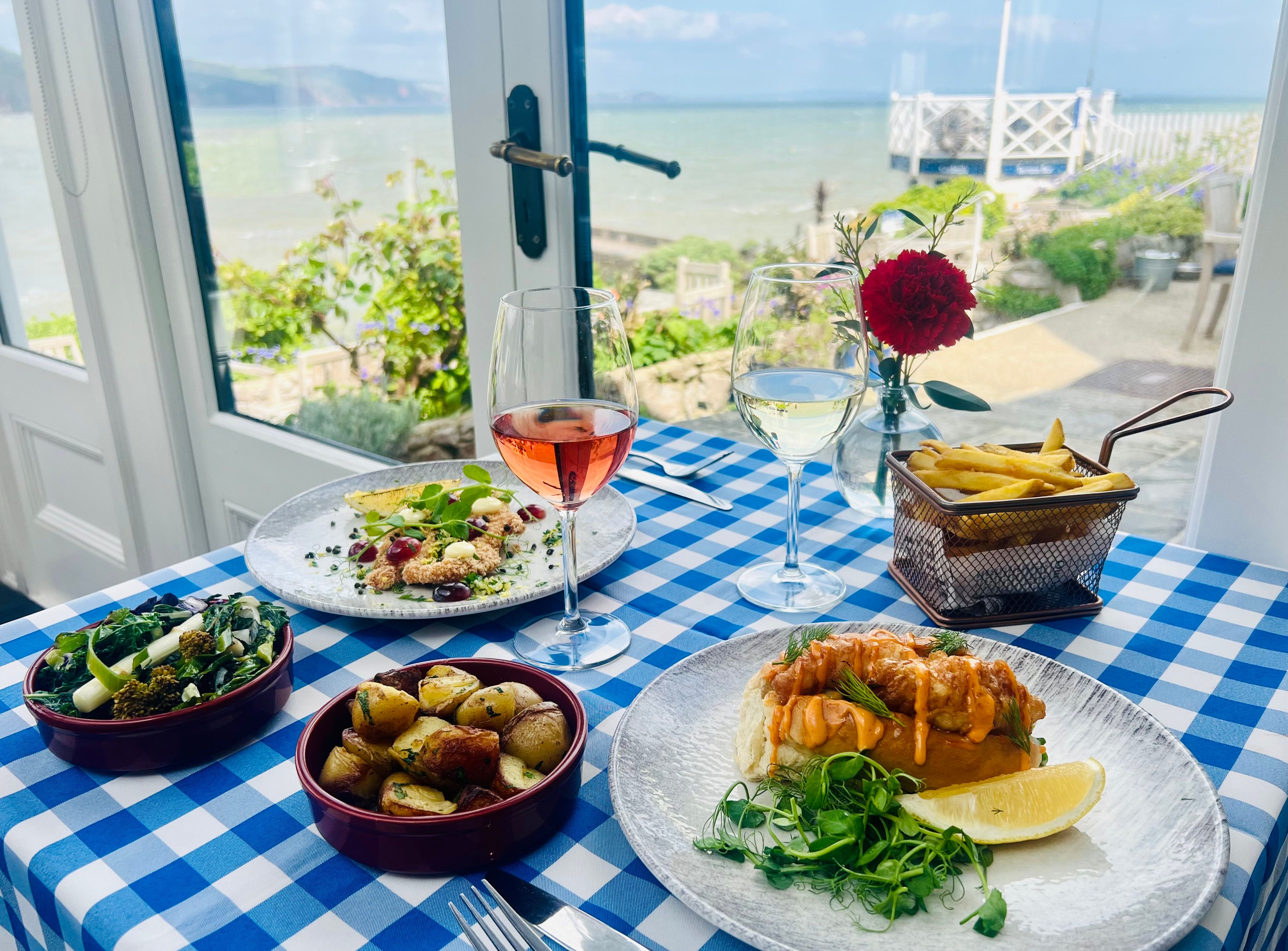 Seafood meal with wine on a blue-and-white checkered table by a window overlooking the sea