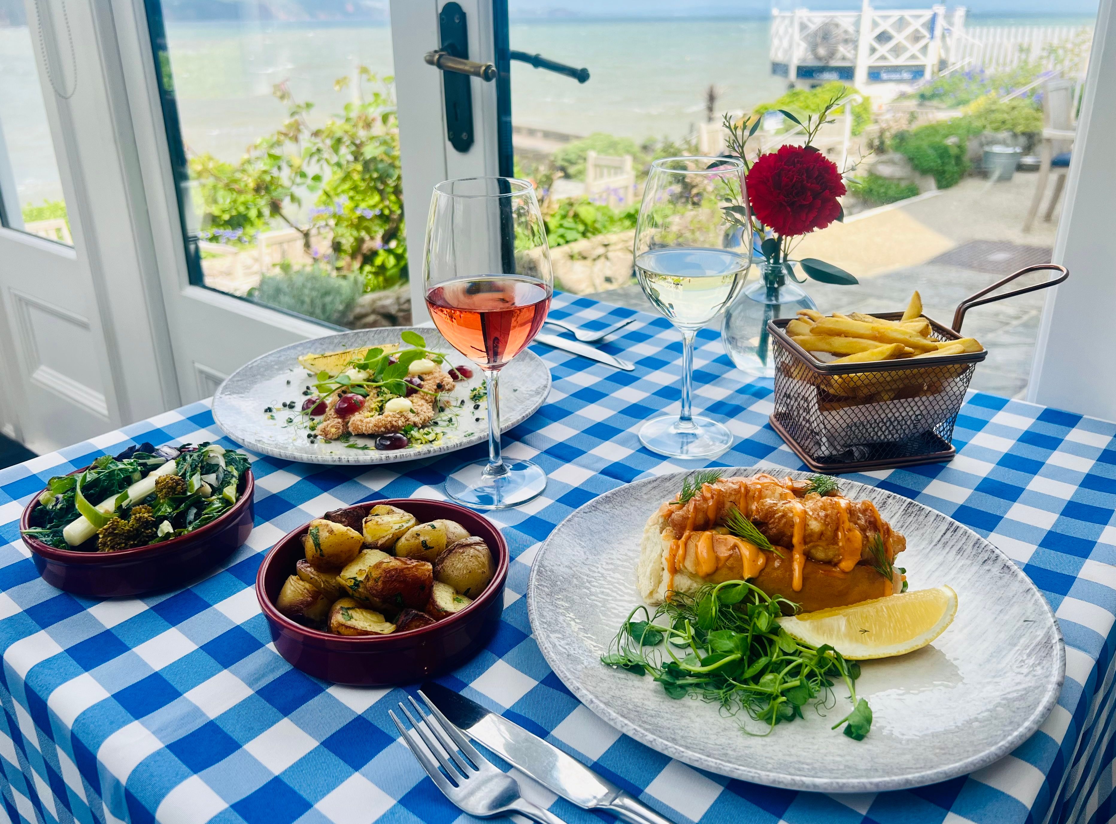 Seafood meal with wine on a blue-and-white checkered table by a window overlooking the sea