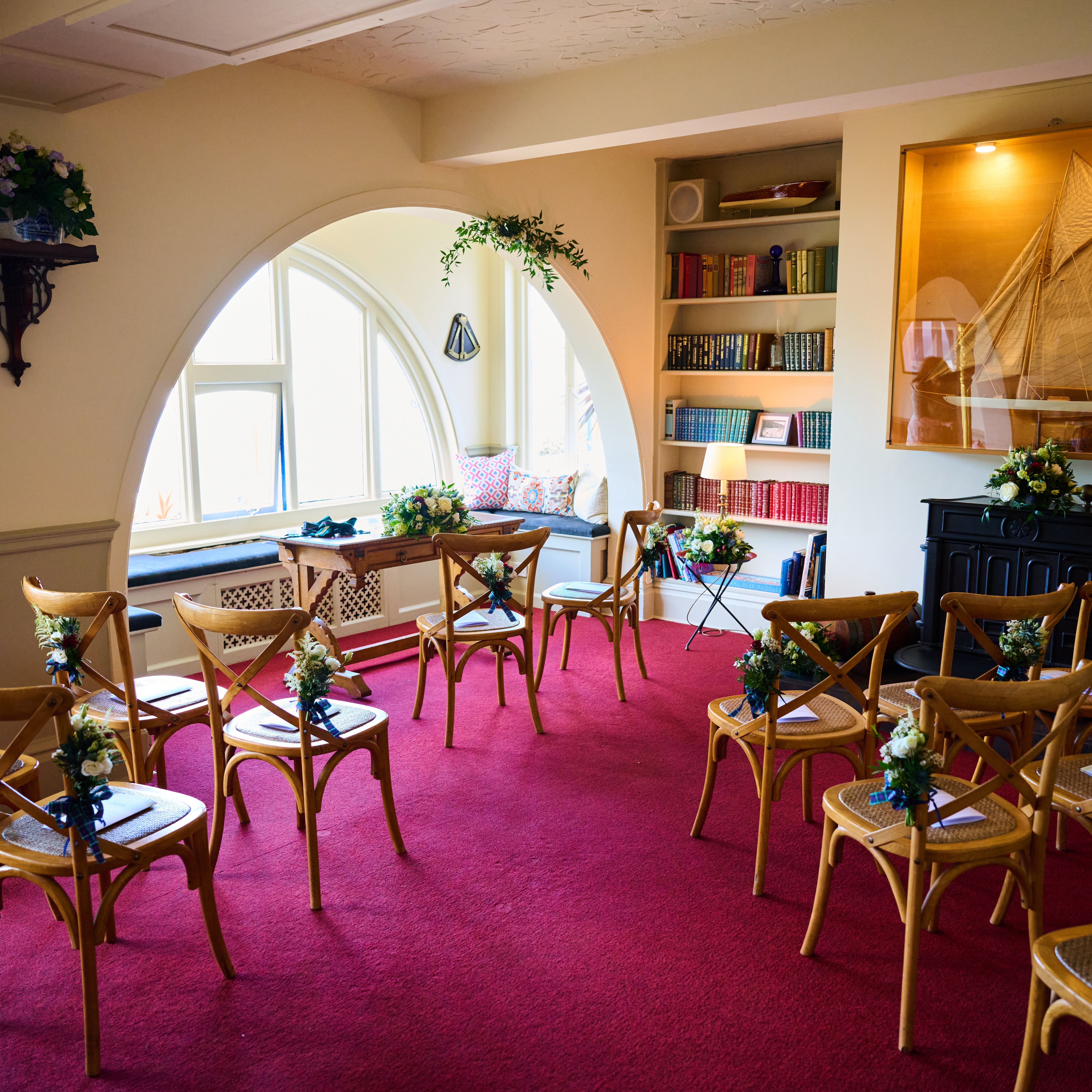 Intimate wedding ceremony room with wooden chairs, floral aisle decorations and arched windows