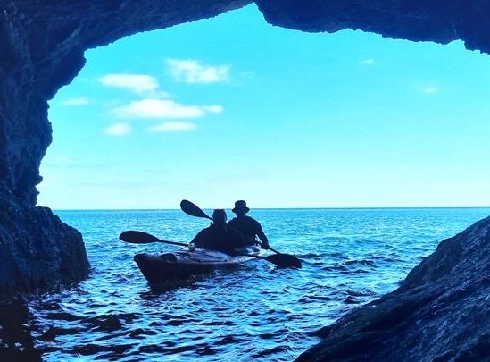 Silhouette of two people kayaking out of a sea cave towards the open ocean