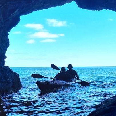 Silhouette of two people kayaking out of a sea cave towards the open ocean