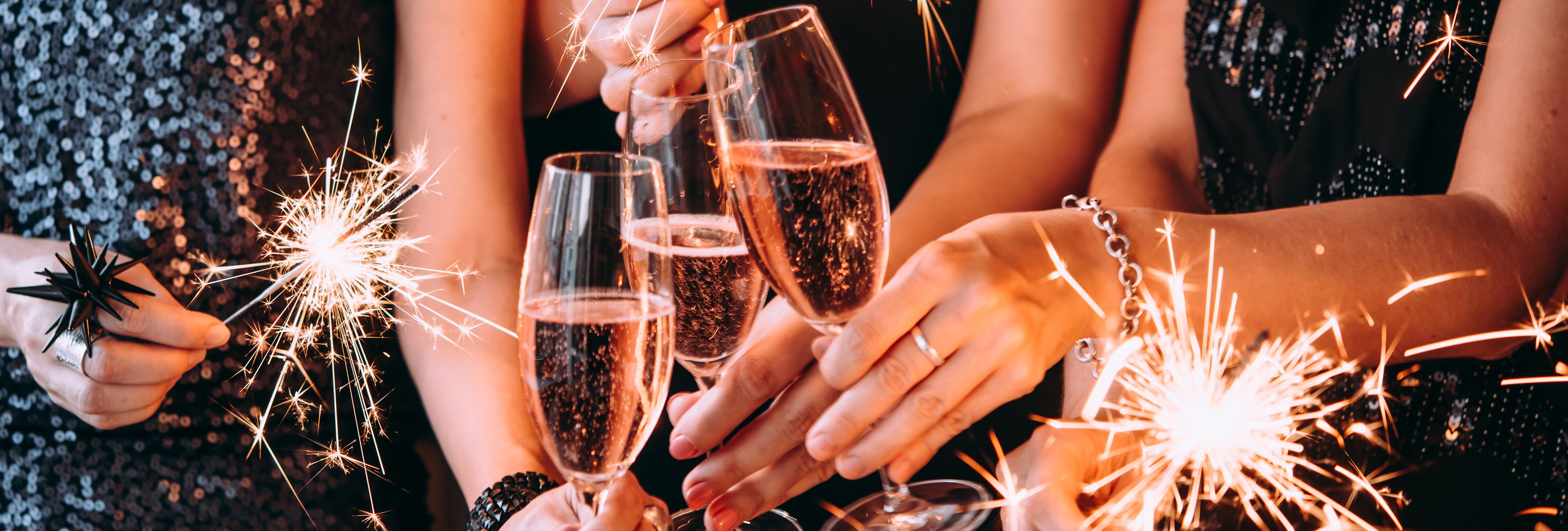 Close-up of people in black sequin outfits holding sparklers and glasses of sparkling wine at a party