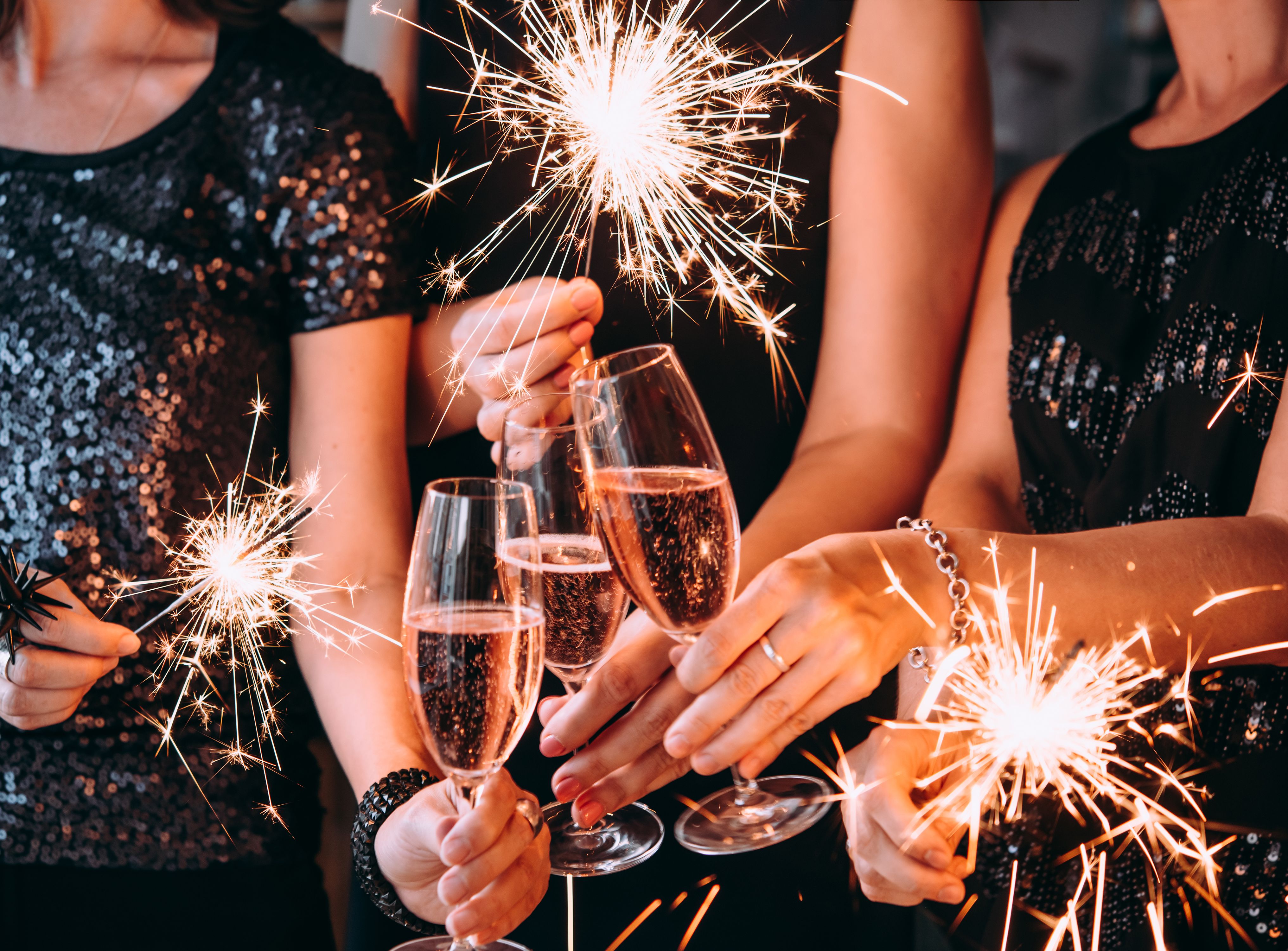 Close-up of people in black sequin outfits holding sparklers and glasses of sparkling wine at a party