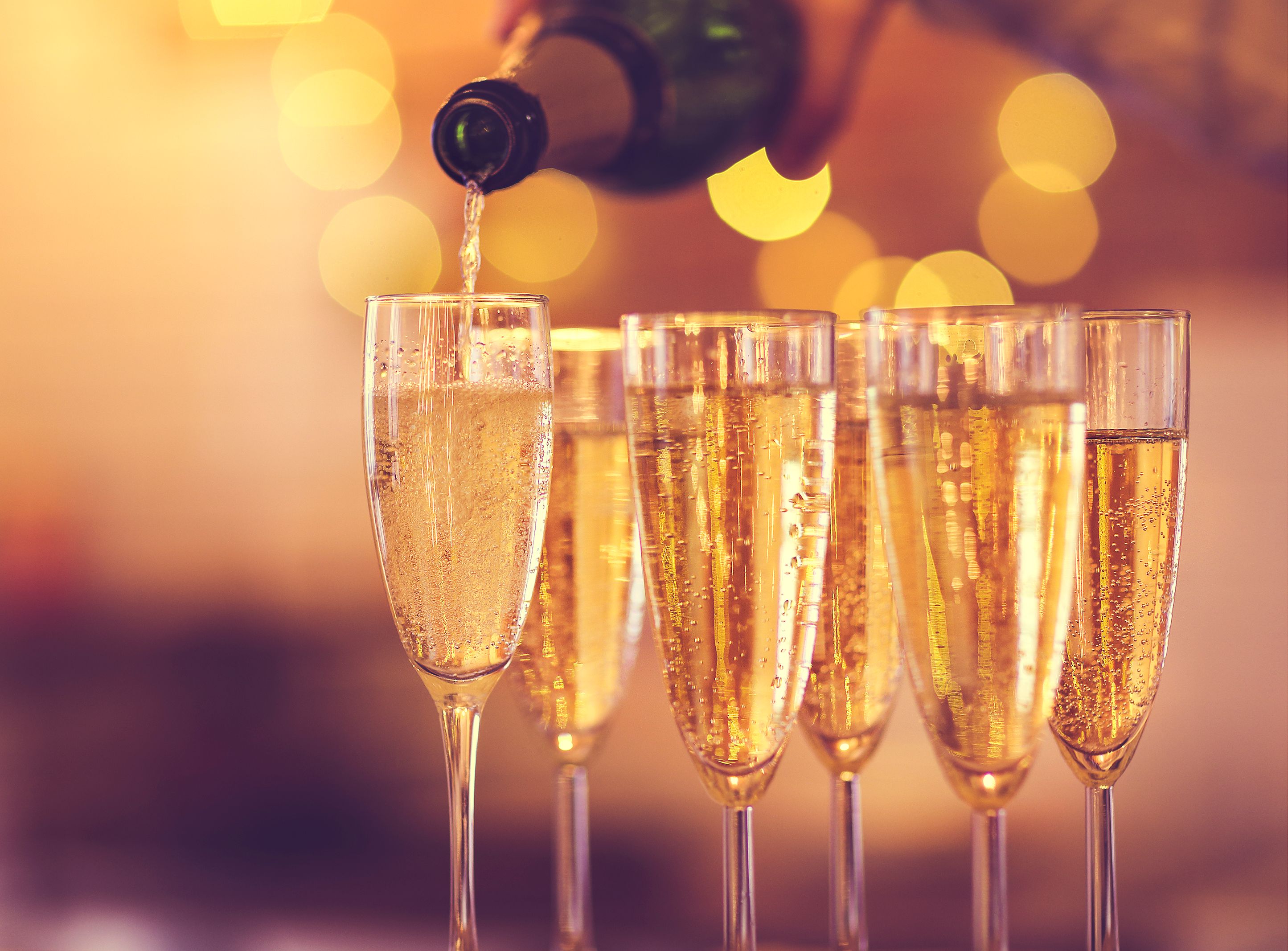Champagne being poured into a flute with several filled glasses in soft, warm bokeh light