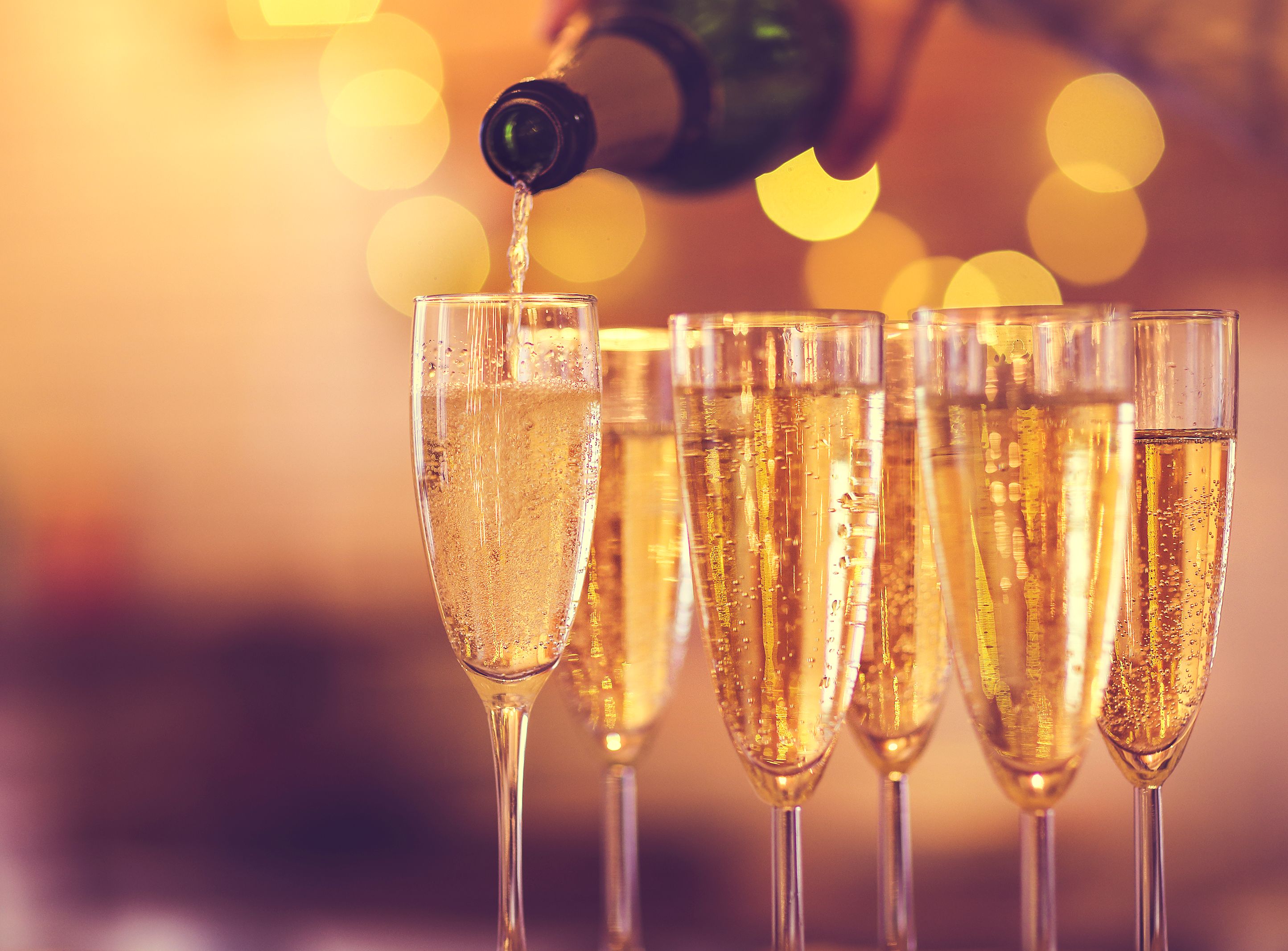 Champagne being poured into a flute with several filled glasses in soft, warm bokeh light