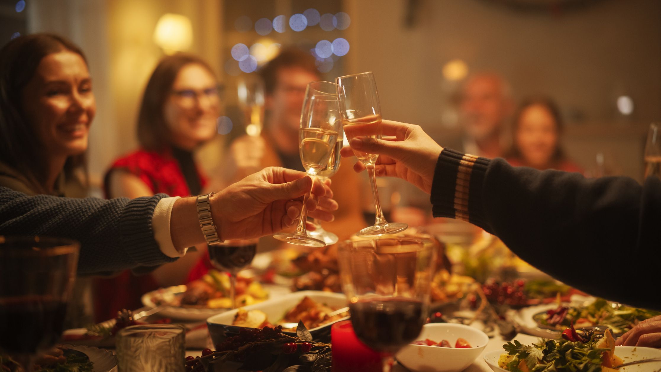 Friends clinking champagne flutes in a toast around a festive dinner table