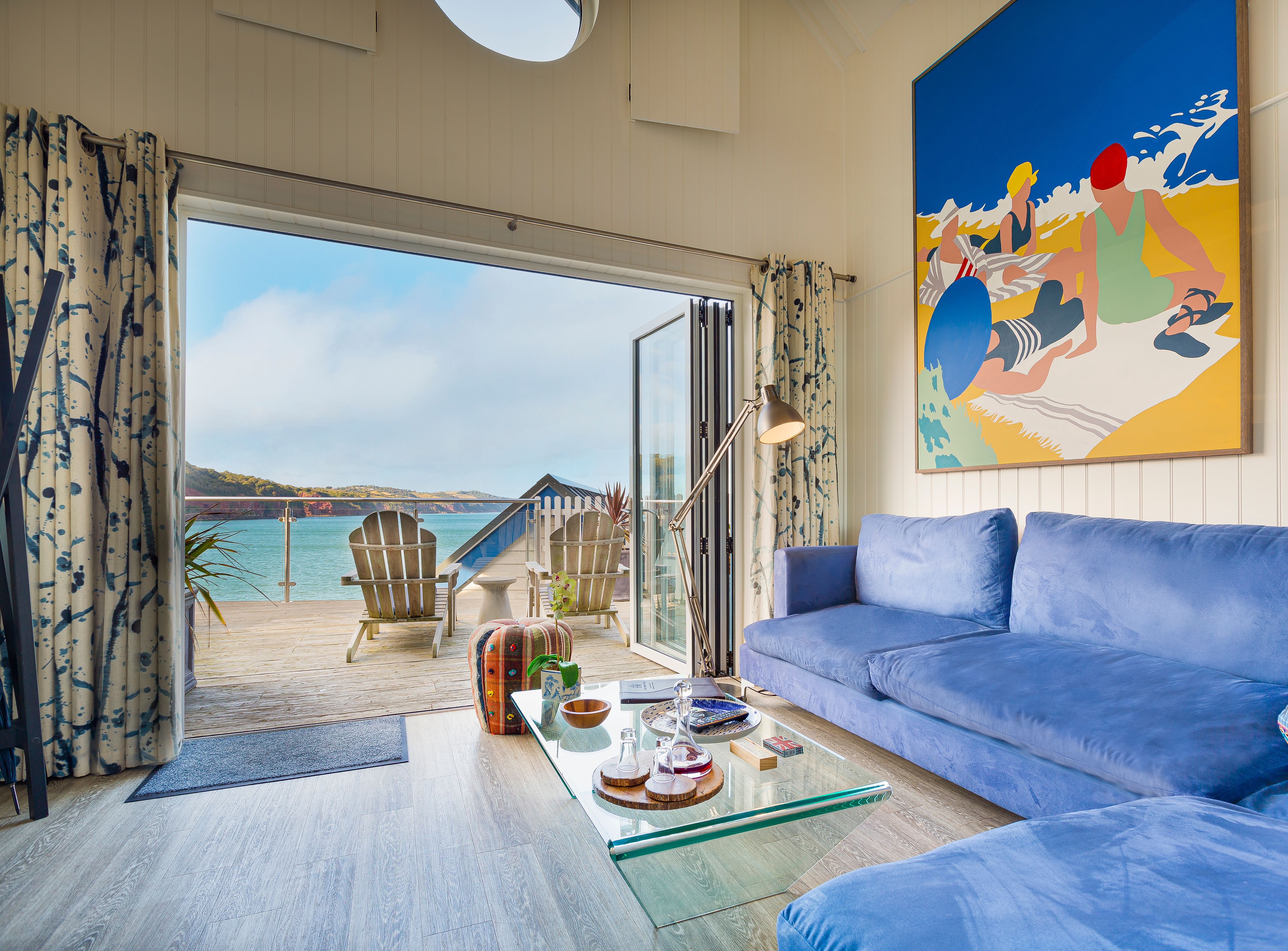 Bright beach hut living room with blue sofa and open doors to a seaside deck
