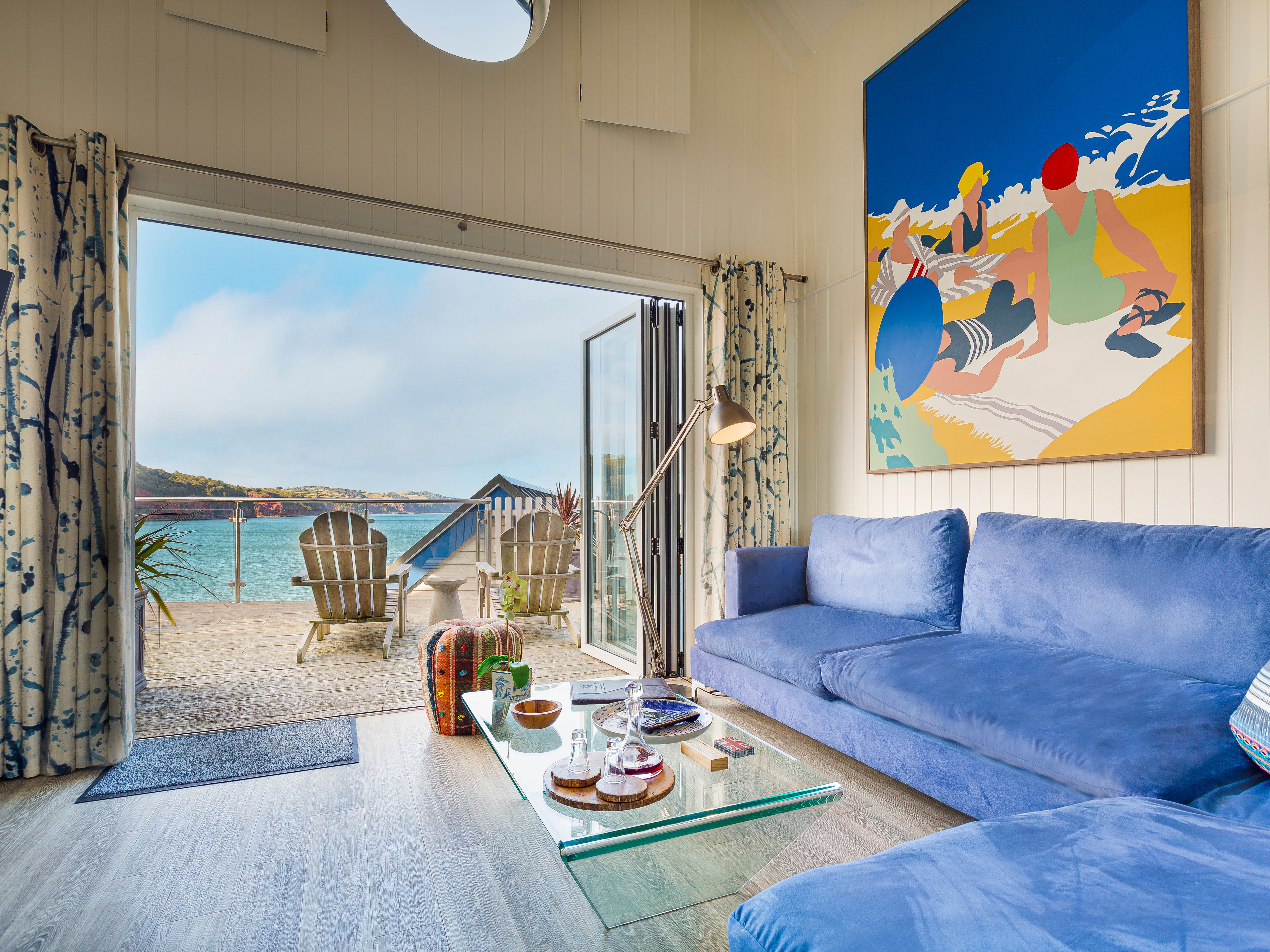 Bright beach hut living room with blue sofa and open doors to a seaside deck