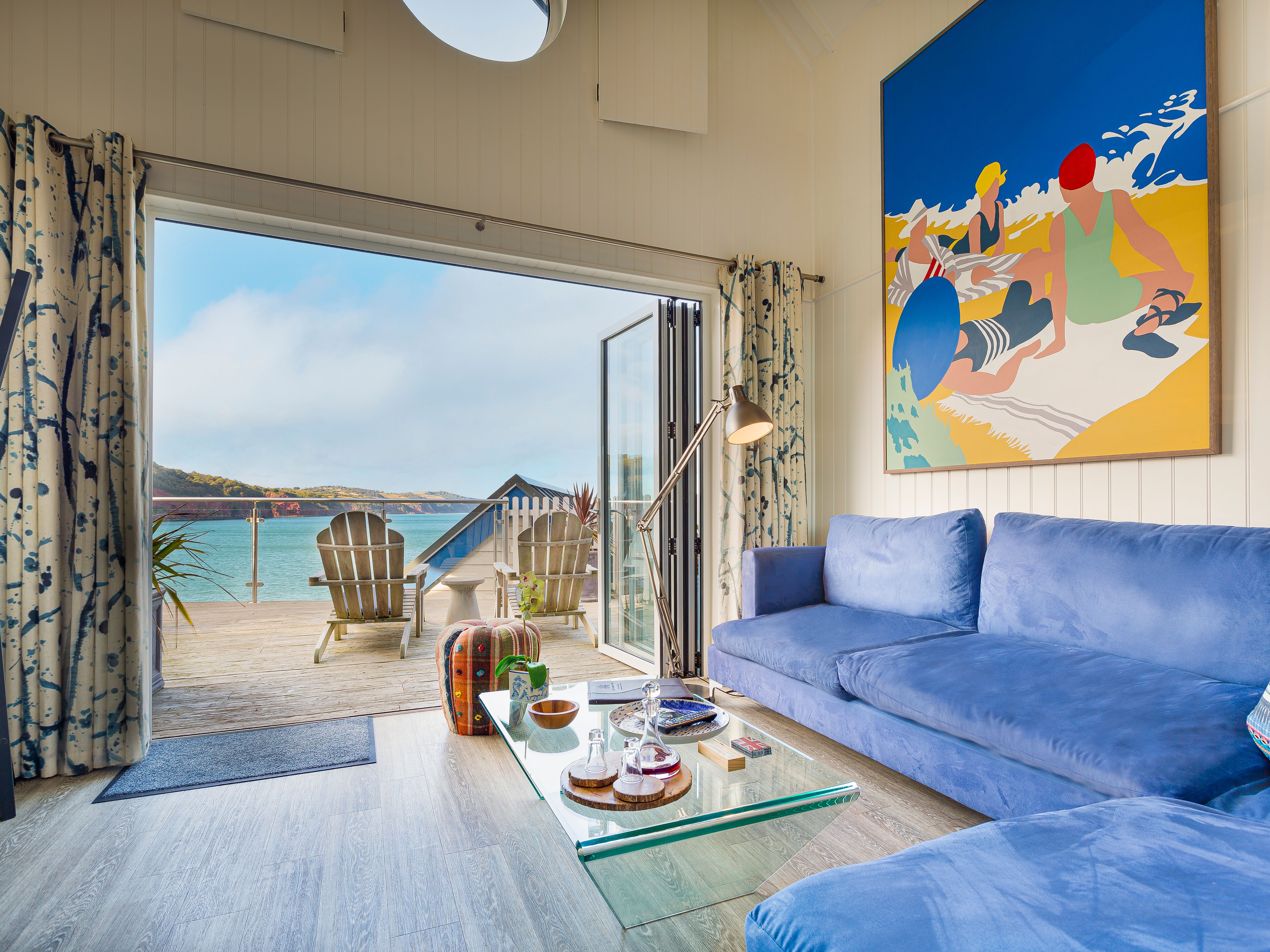 Bright beach hut living room with blue sofa and open doors to a seaside deck