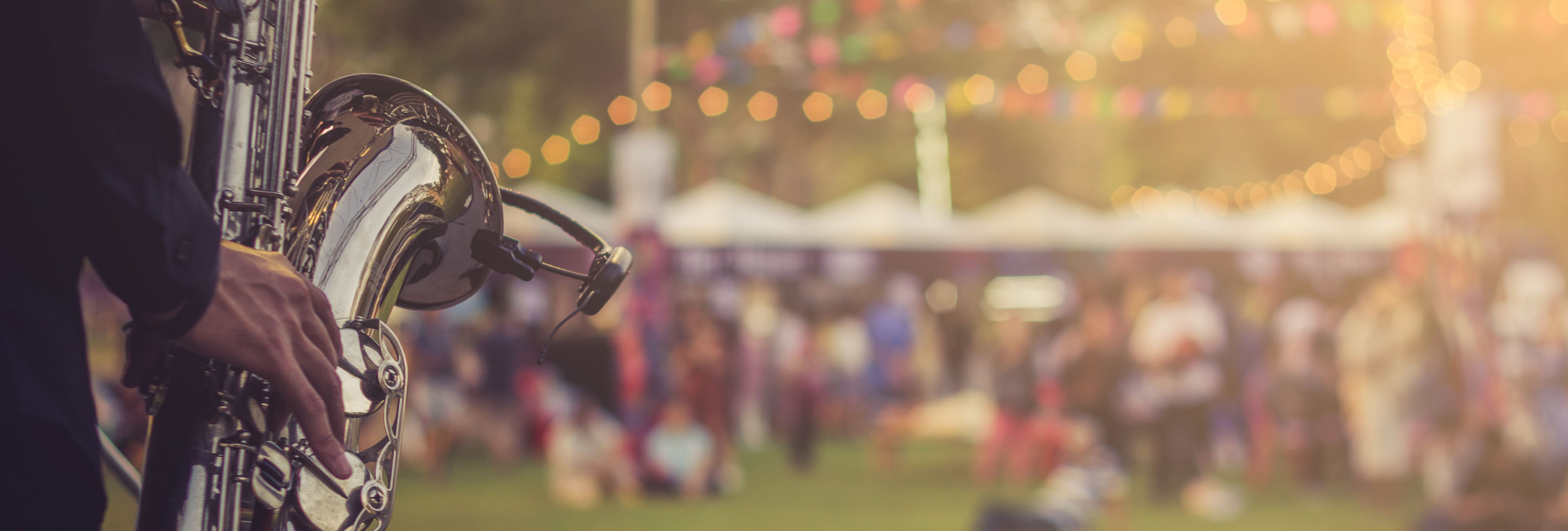 Close-up of a musician holding a saxophone on an outdoor stage with festival lights and a blurred crowd in the background