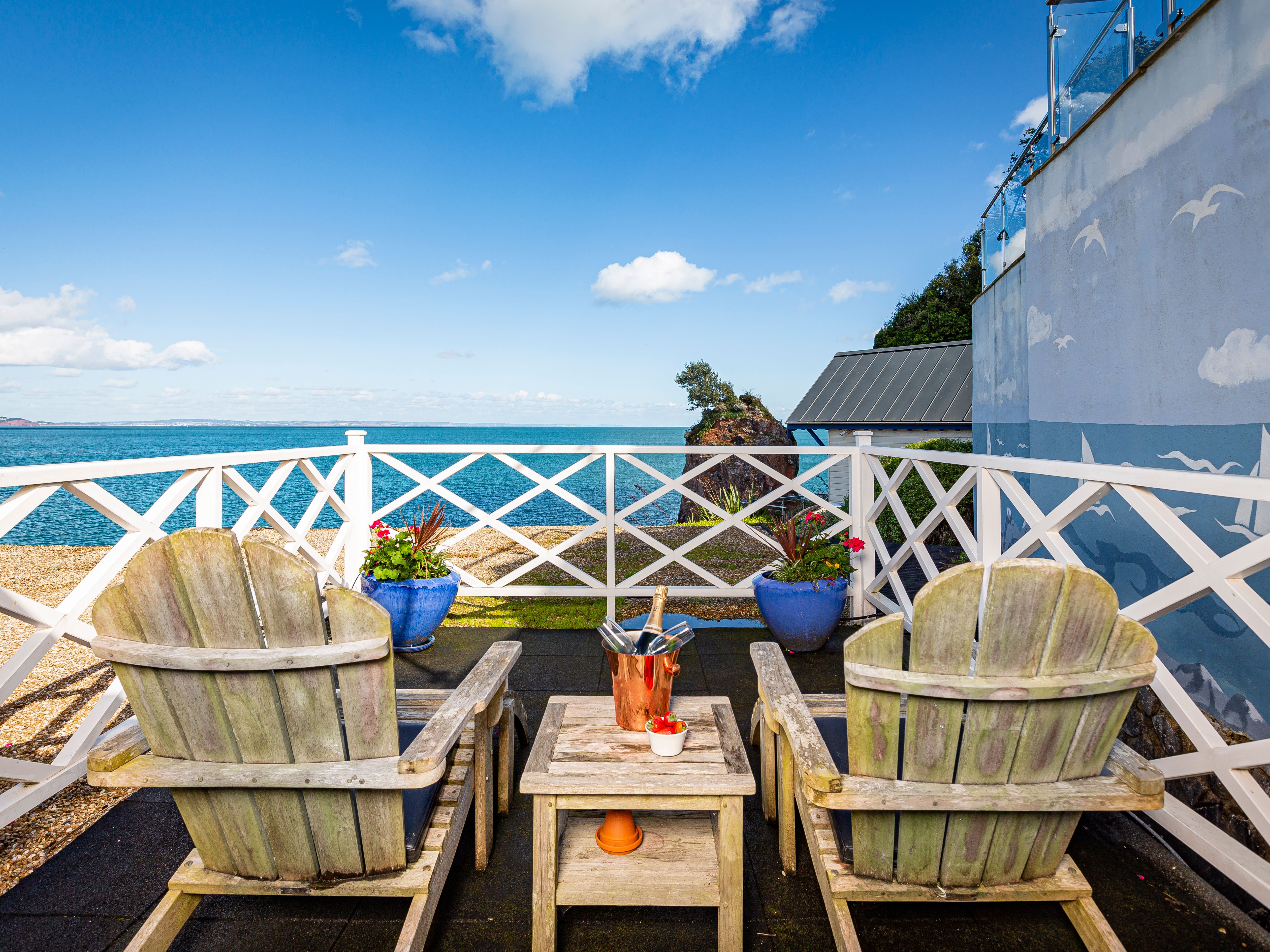 Seaside terrace with two wooden Adirondack chairs overlooking the sea, with a table holding an ice bucket and strawberries