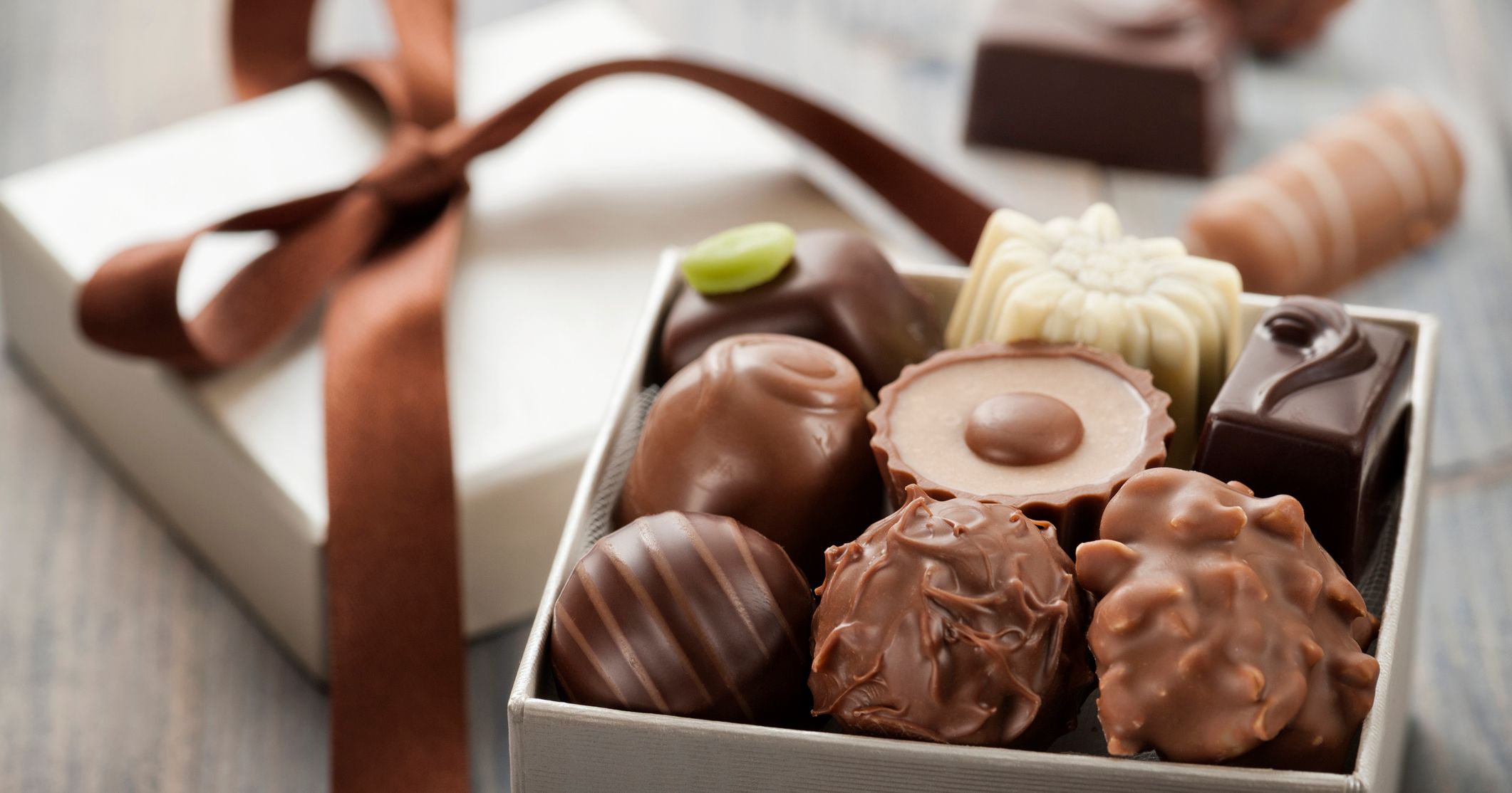 Assorted chocolates in an open gift box with a brown ribbon on a wooden table
