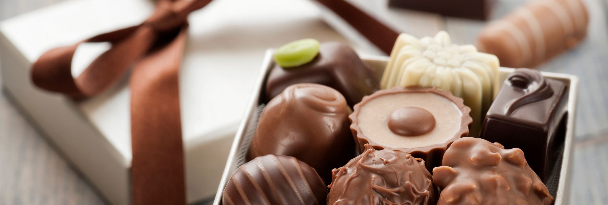 Assorted chocolates in an open gift box with a brown ribbon on a wooden table