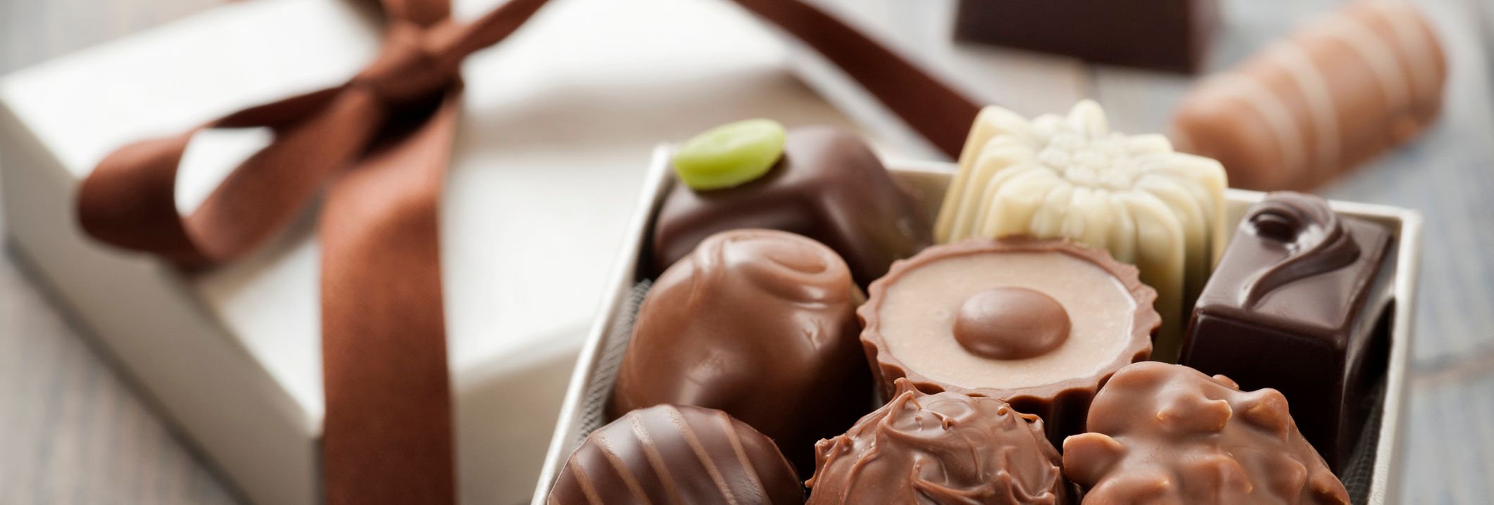 Assorted chocolates in an open gift box with a brown ribbon on a wooden table