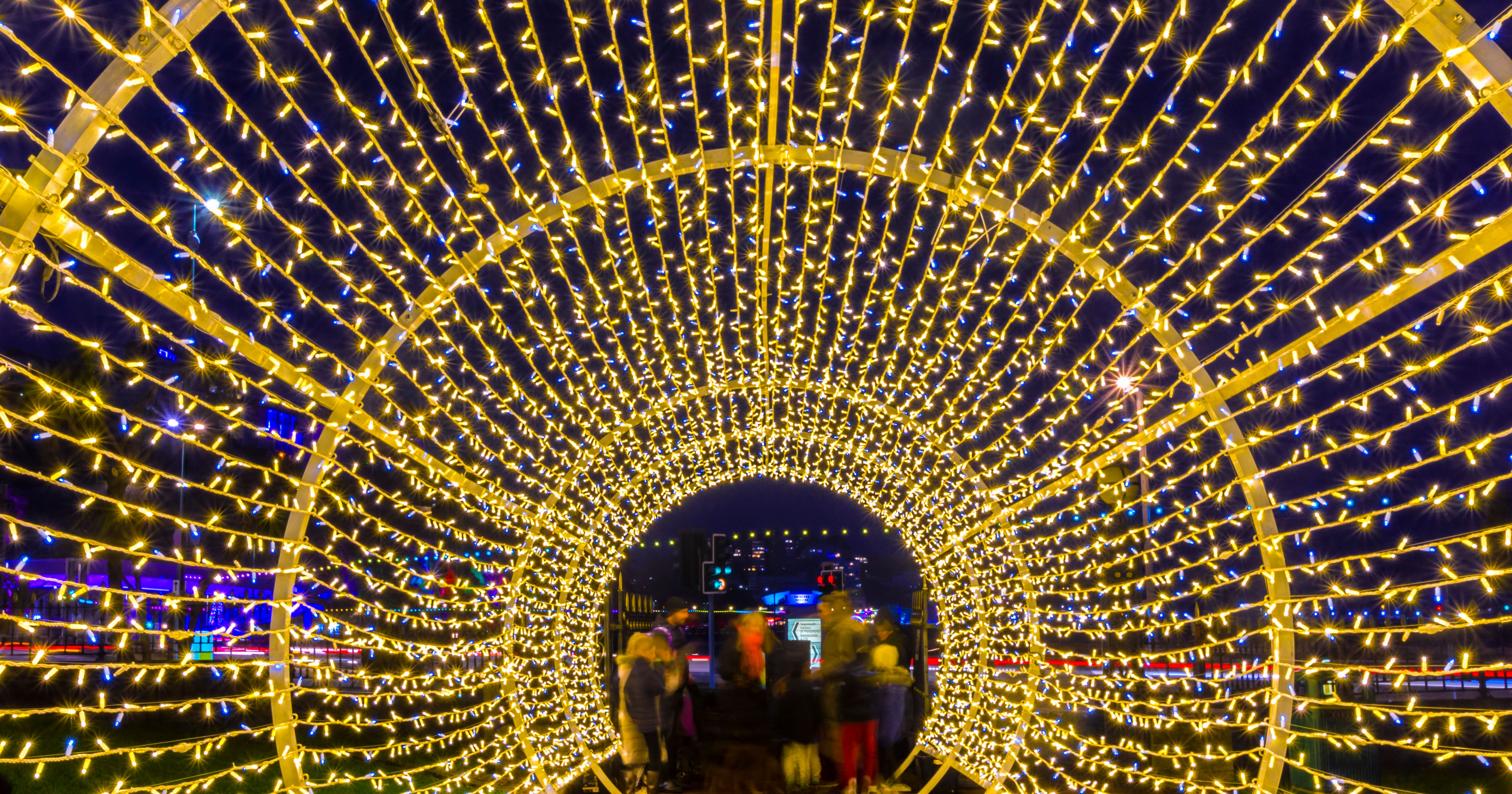 People walking through a tunnel of golden and blue fairy lights at night during Bay of Lights 2023