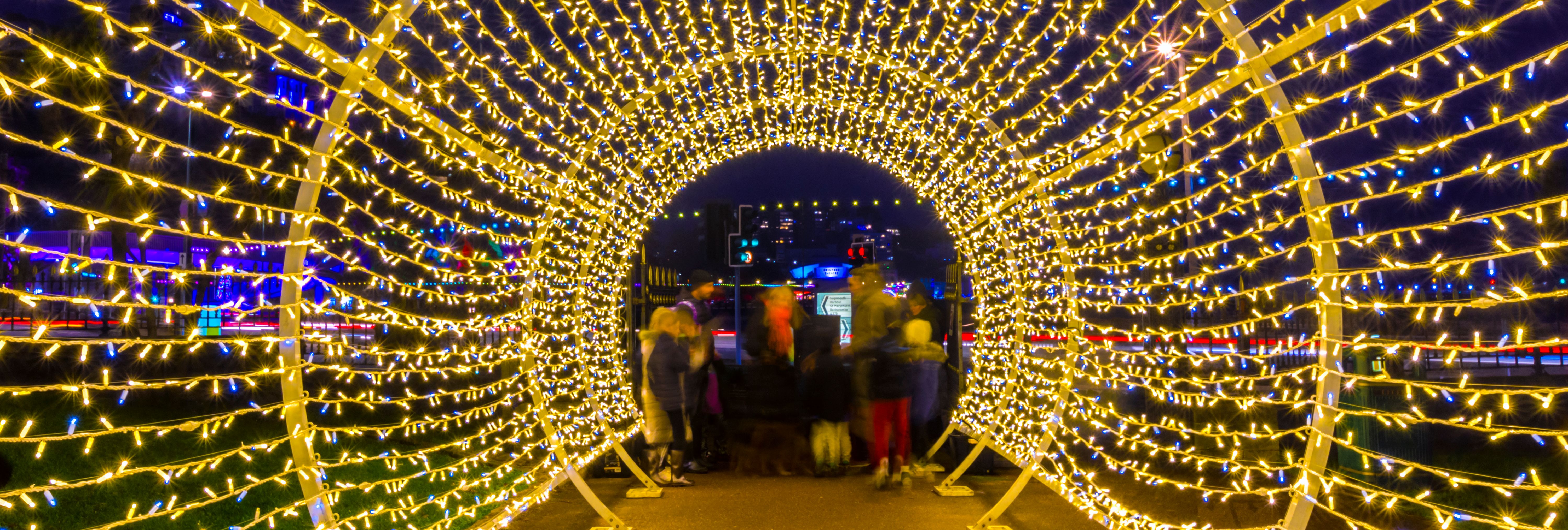 People walking through a tunnel of golden and blue fairy lights at night during Bay of Lights 2023