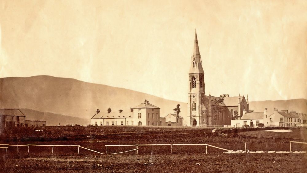 Castle House and Chapel with a tall steeple, surrounded by other buildings and hills in the background, 1890.
