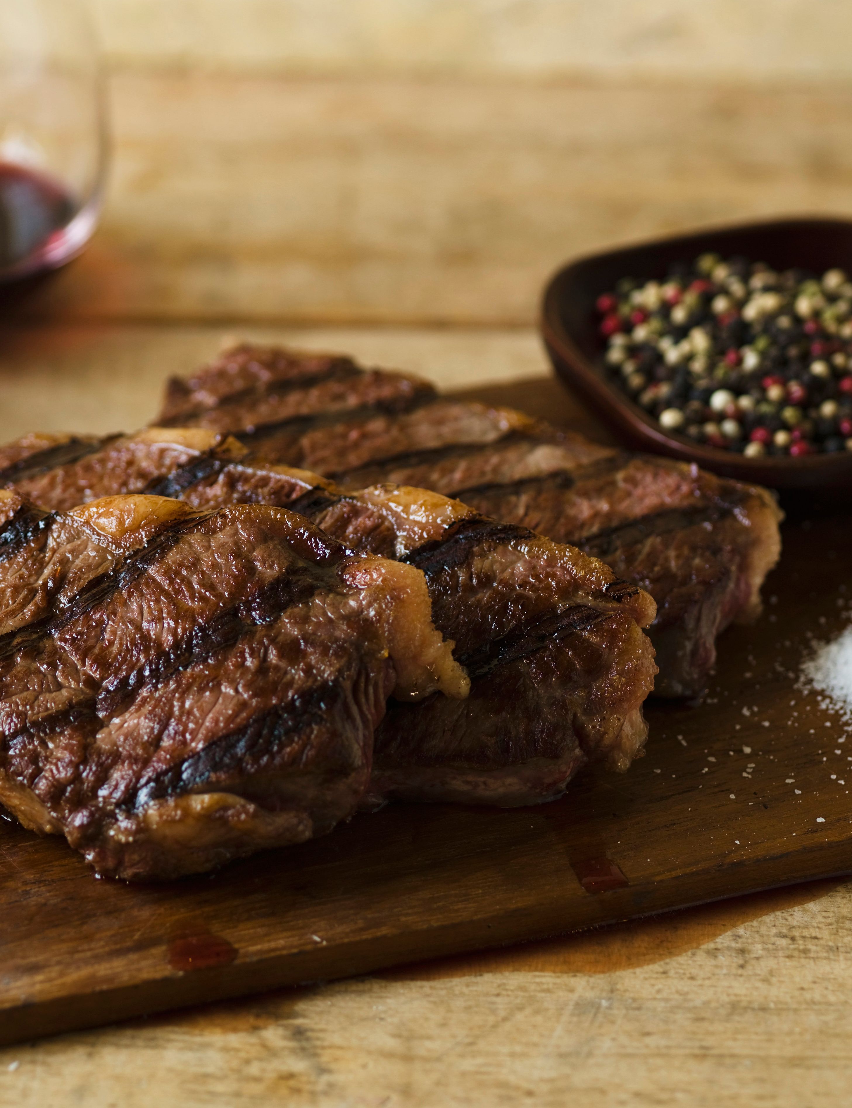 Grilled steak on a wooden cutting board with salt, pepper, and red wine