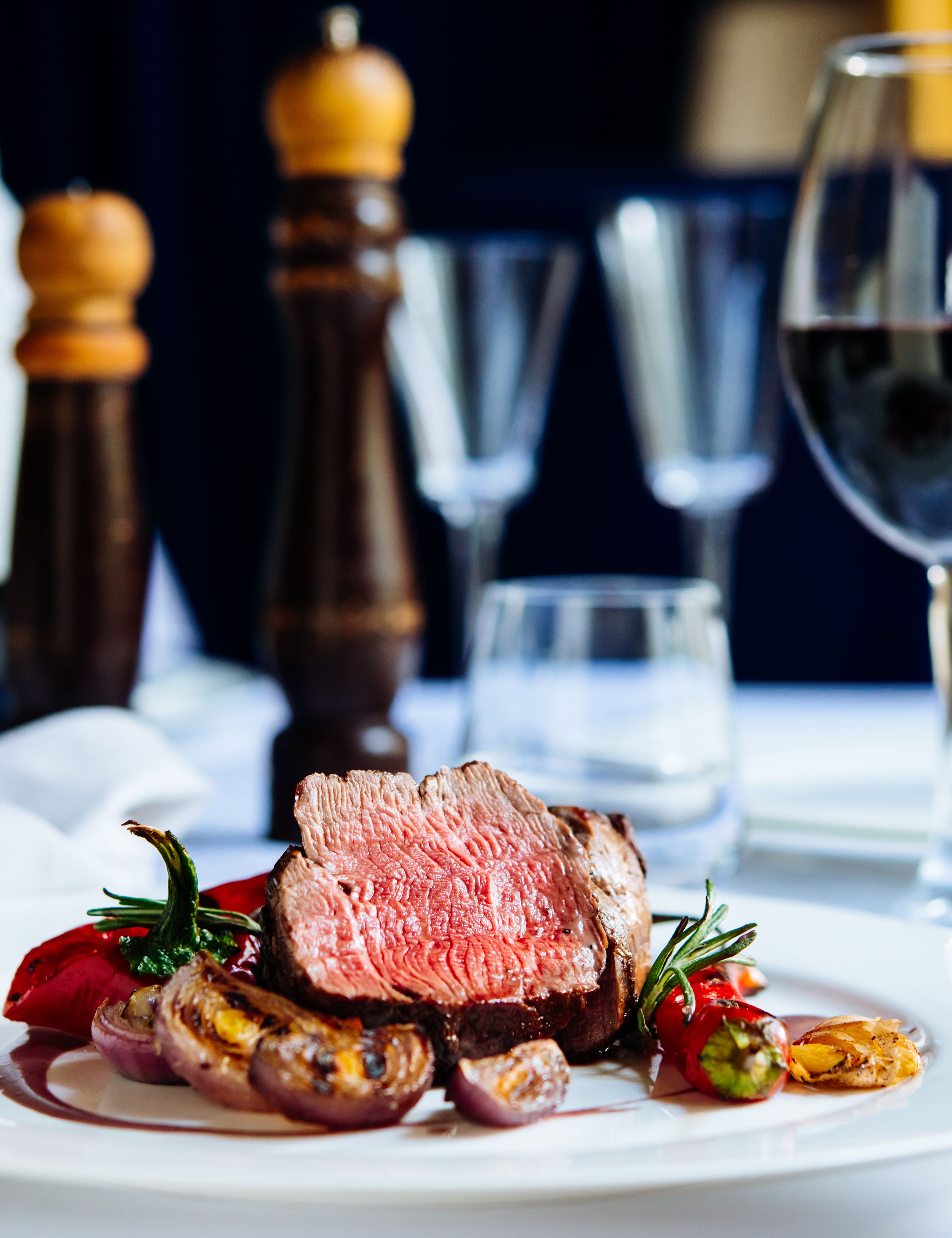 A gourmet steak dish served with grilled vegetables and a glass of red wine on an elegant restaurant table.