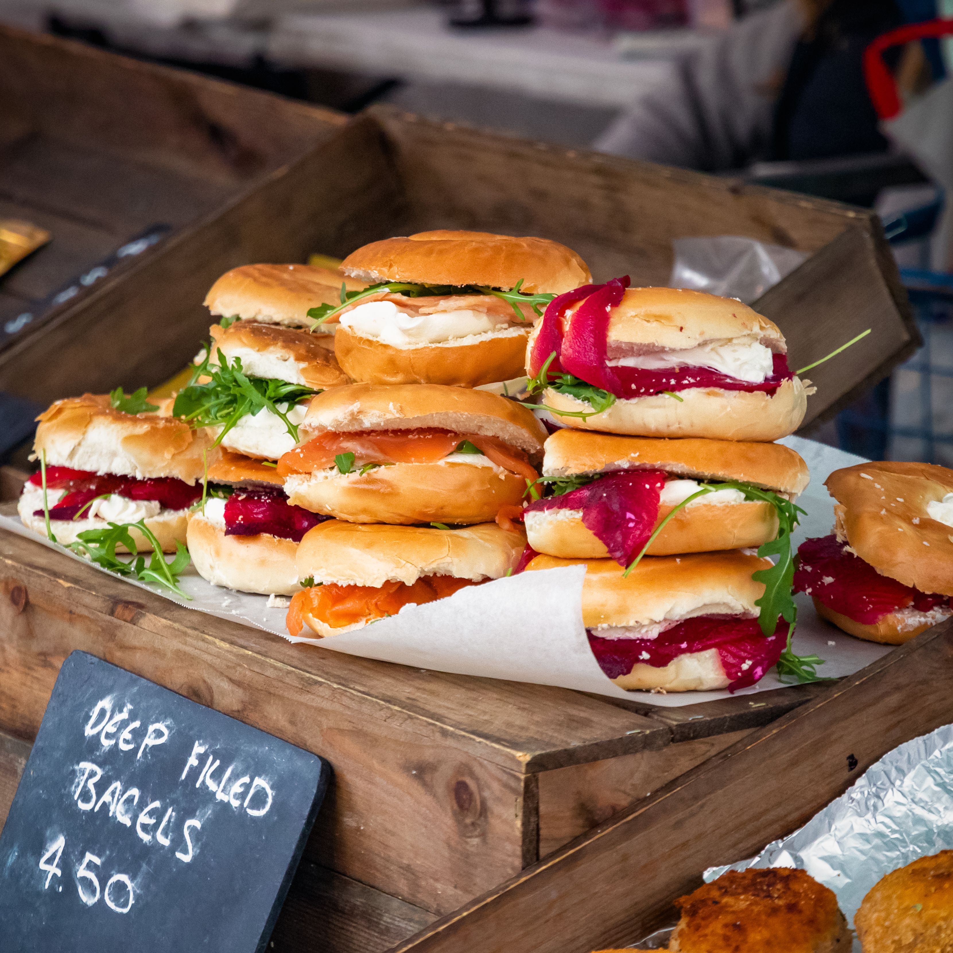 A display of deep filled bagels with cream cheese, vegetables, and greens at a market stall