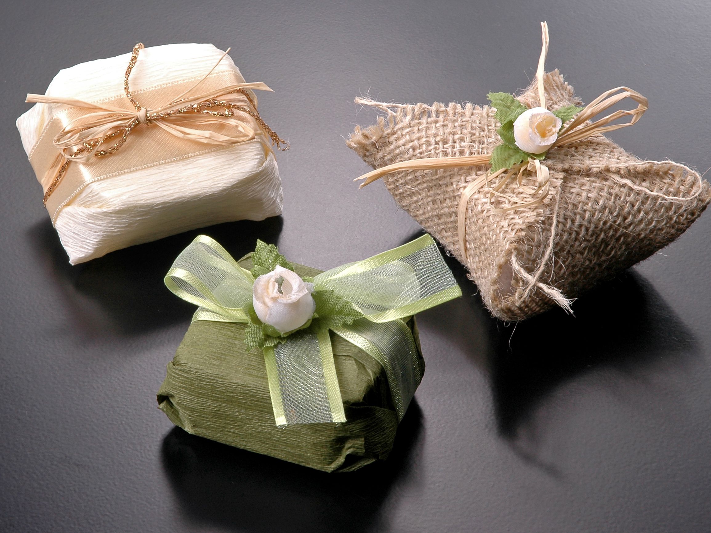 Three small decorative gift boxes wrapped in different textured fabrics and adorned with ribbon and artificial flowers.