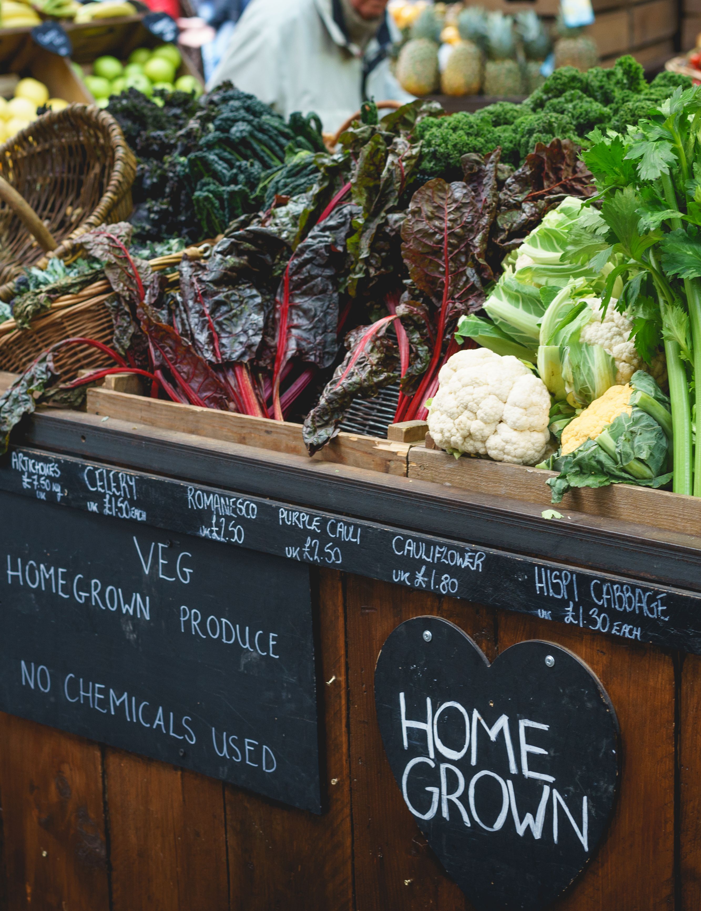 Fresh organic vegetables displayed at a local farmers market stall with signs reading 'home grown' and 'no chemicals used'.