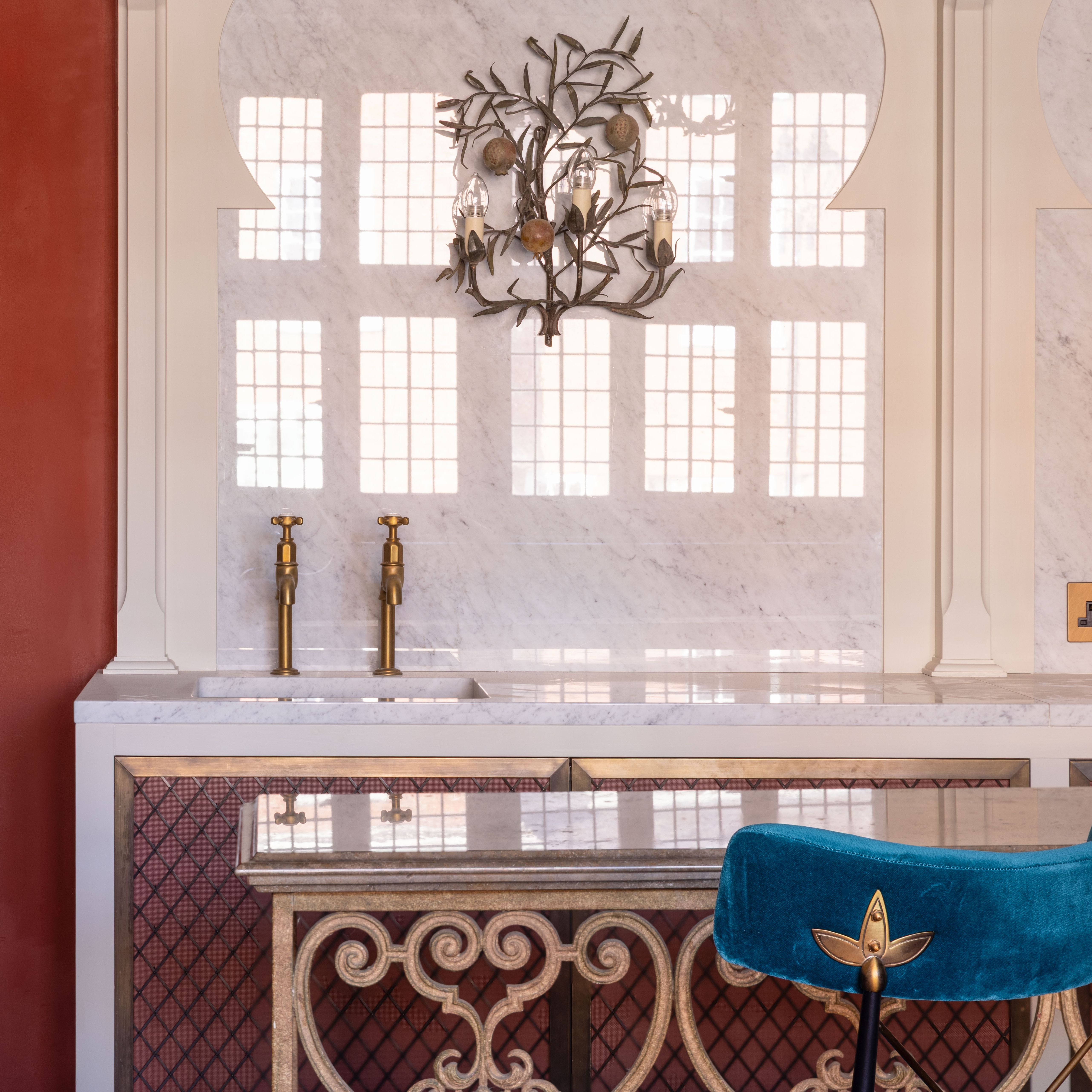 Elegant kitchen area with marble countertop, gold fixtures, and a blue velvet chair.